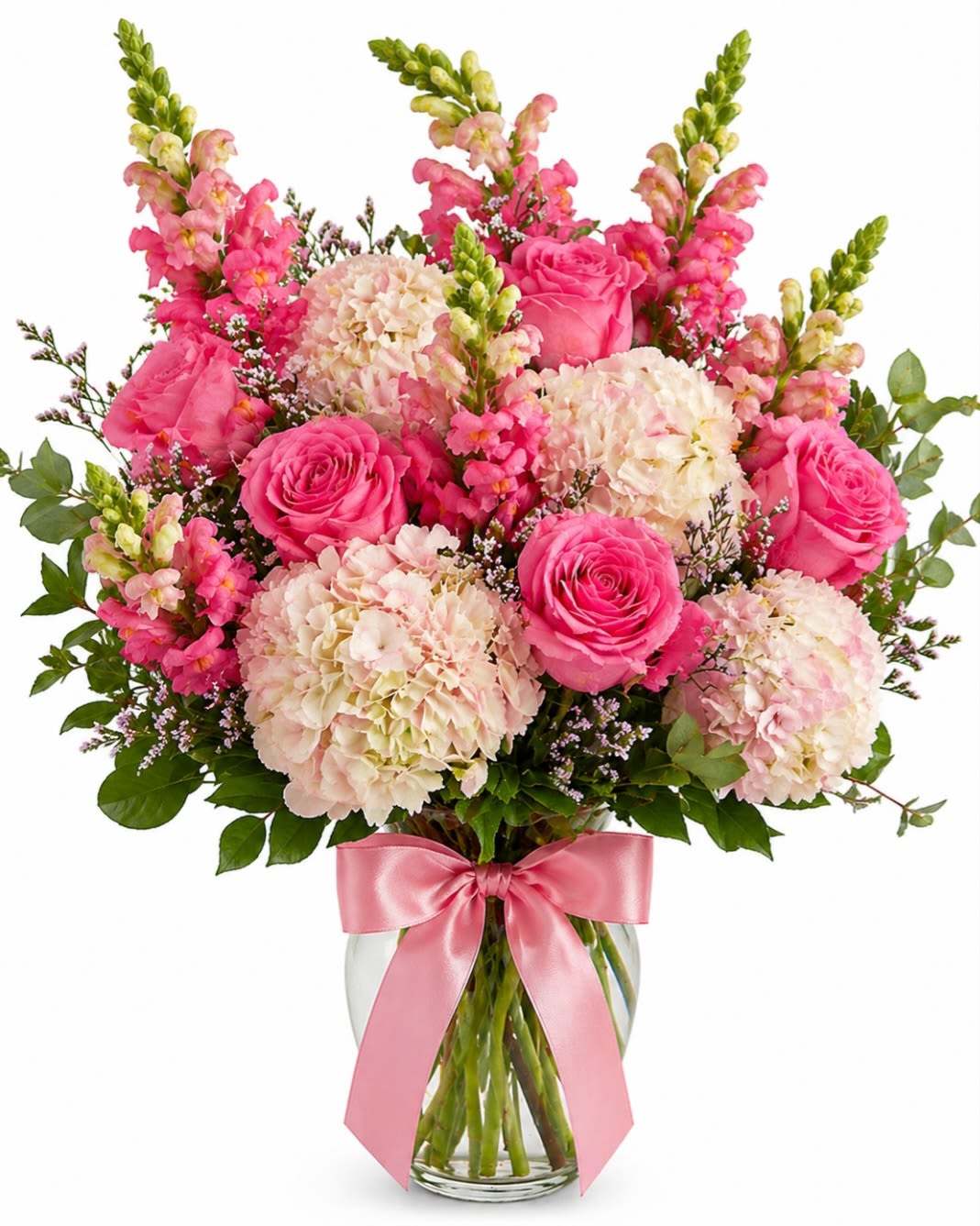 Rosy Garden Grace - A lush everyday arrangement featuring elegant pink roses, cloud like hydrangea blooms and gracefully snap dragons accented with fresh greenery and delicate filler flowers. Designed in a clear glass vase and finished with a satin pink bow.