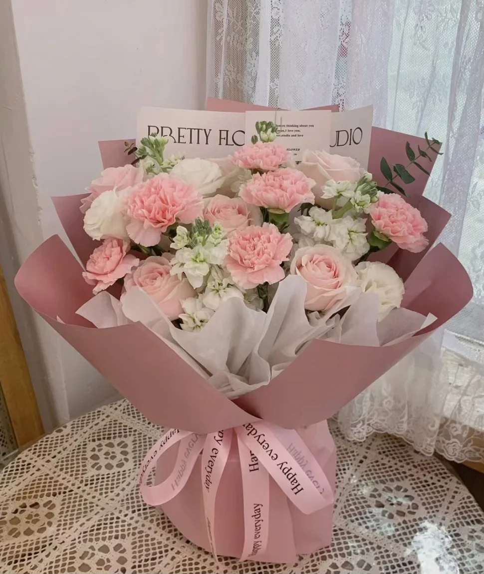 Pink and white bouquet of roses and carnations wrapped in pink paper