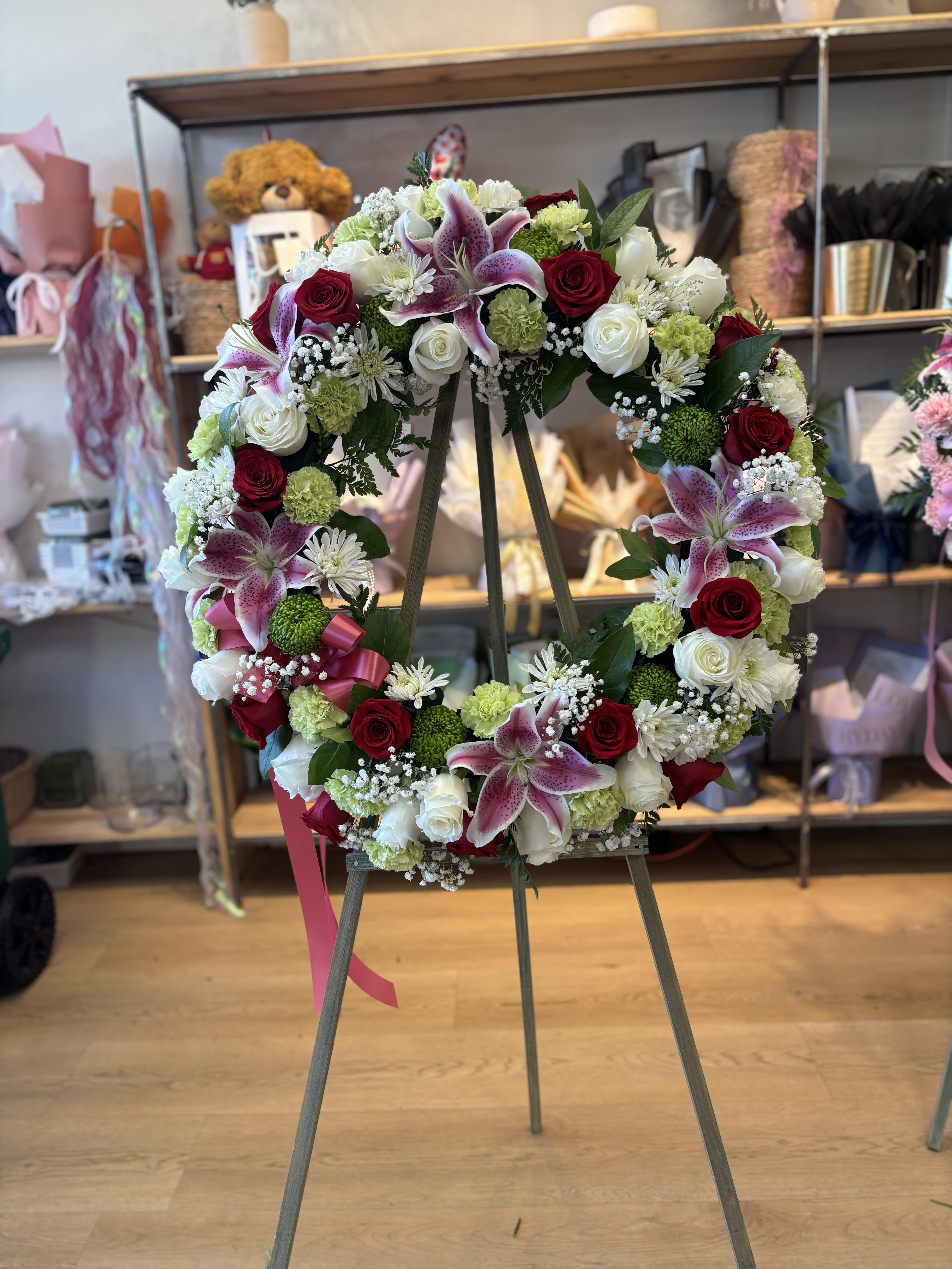Circular floral wreath on an easel with red, white, and pink blooms