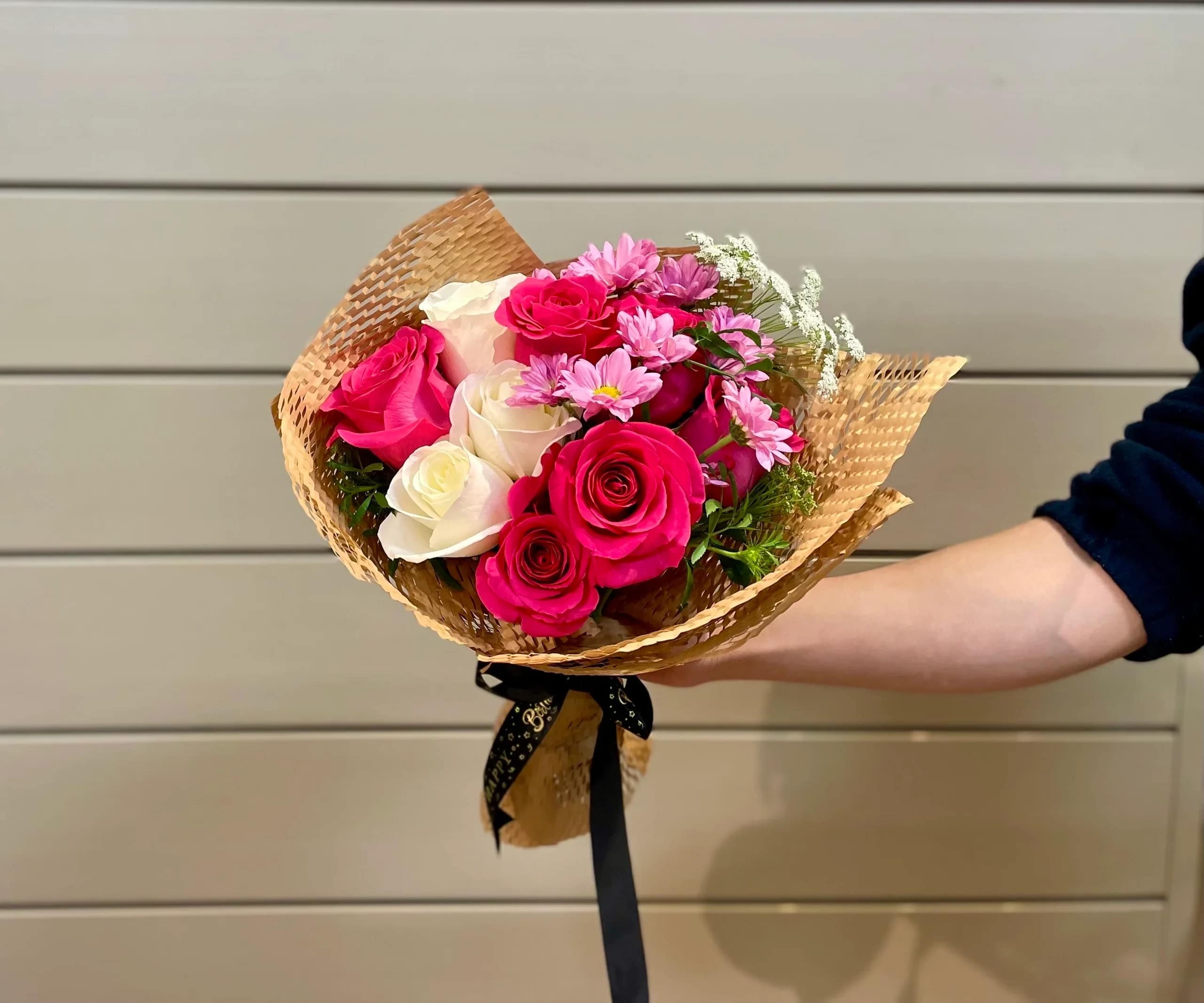 Handheld bouquet of pink and white roses with small pink daisies