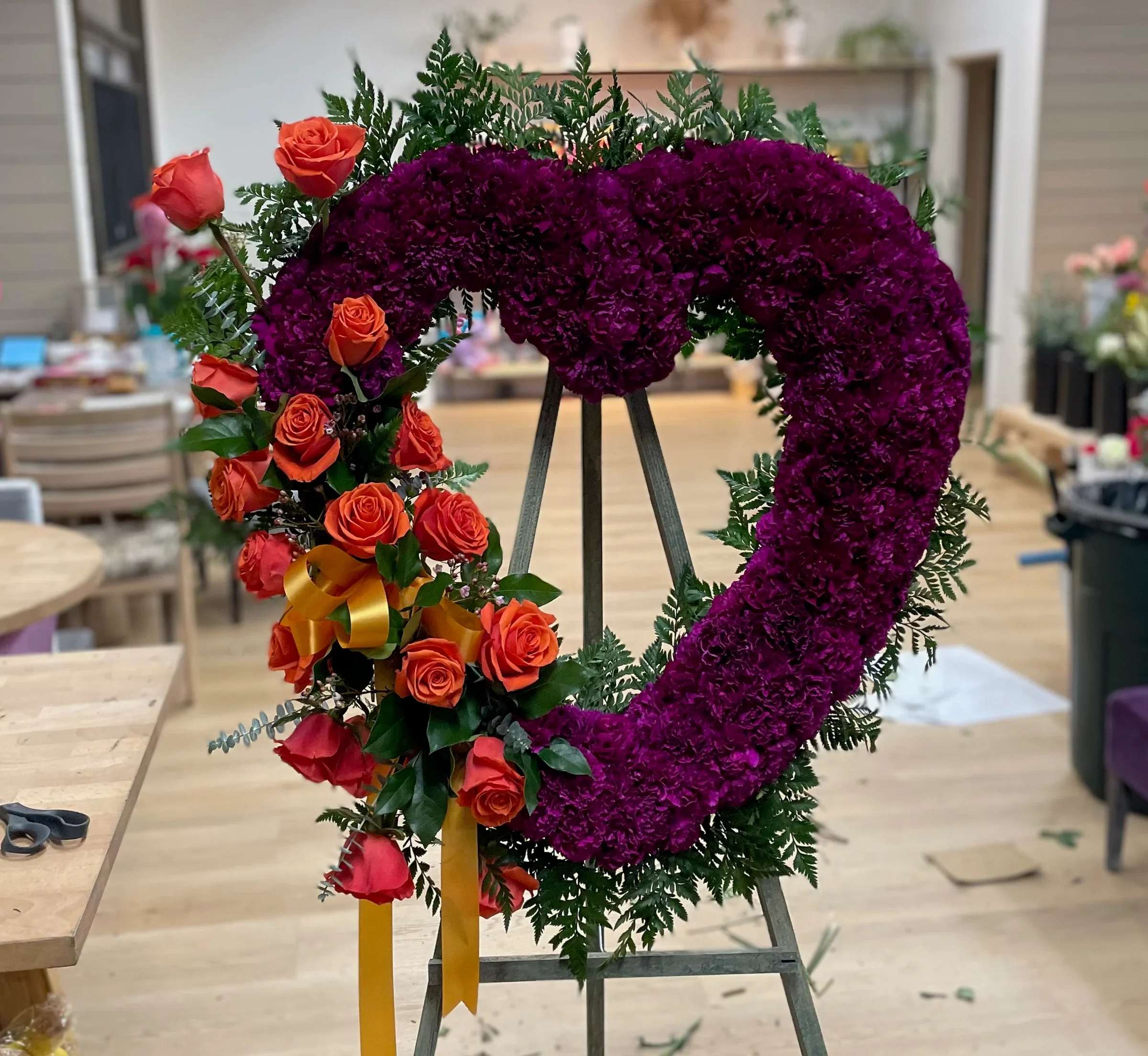 Heart-shaped floral wreath with purple blooms and orange roses on an easel