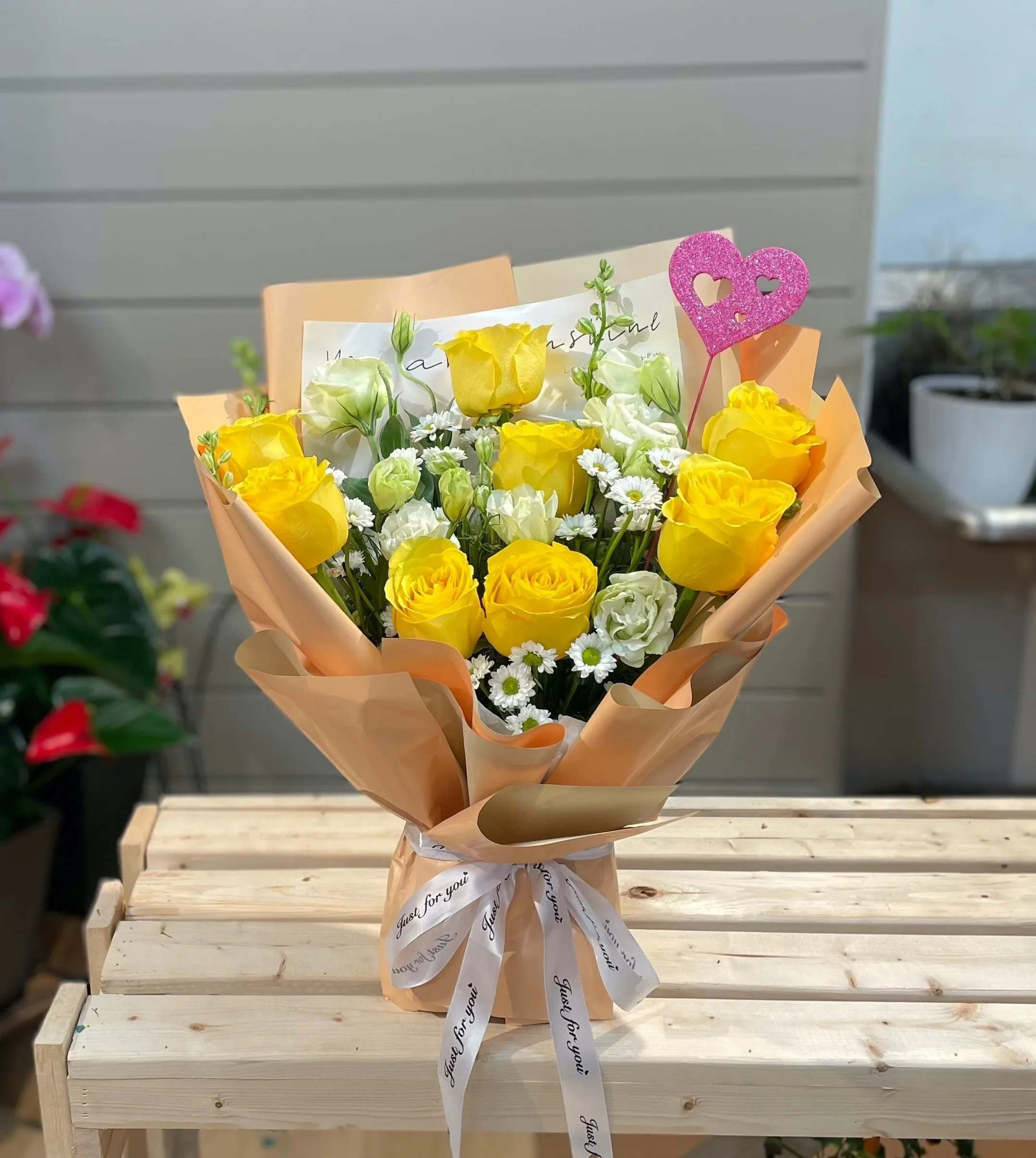 Yellow roses and white flowers in peach wrapping with a pink heart topper