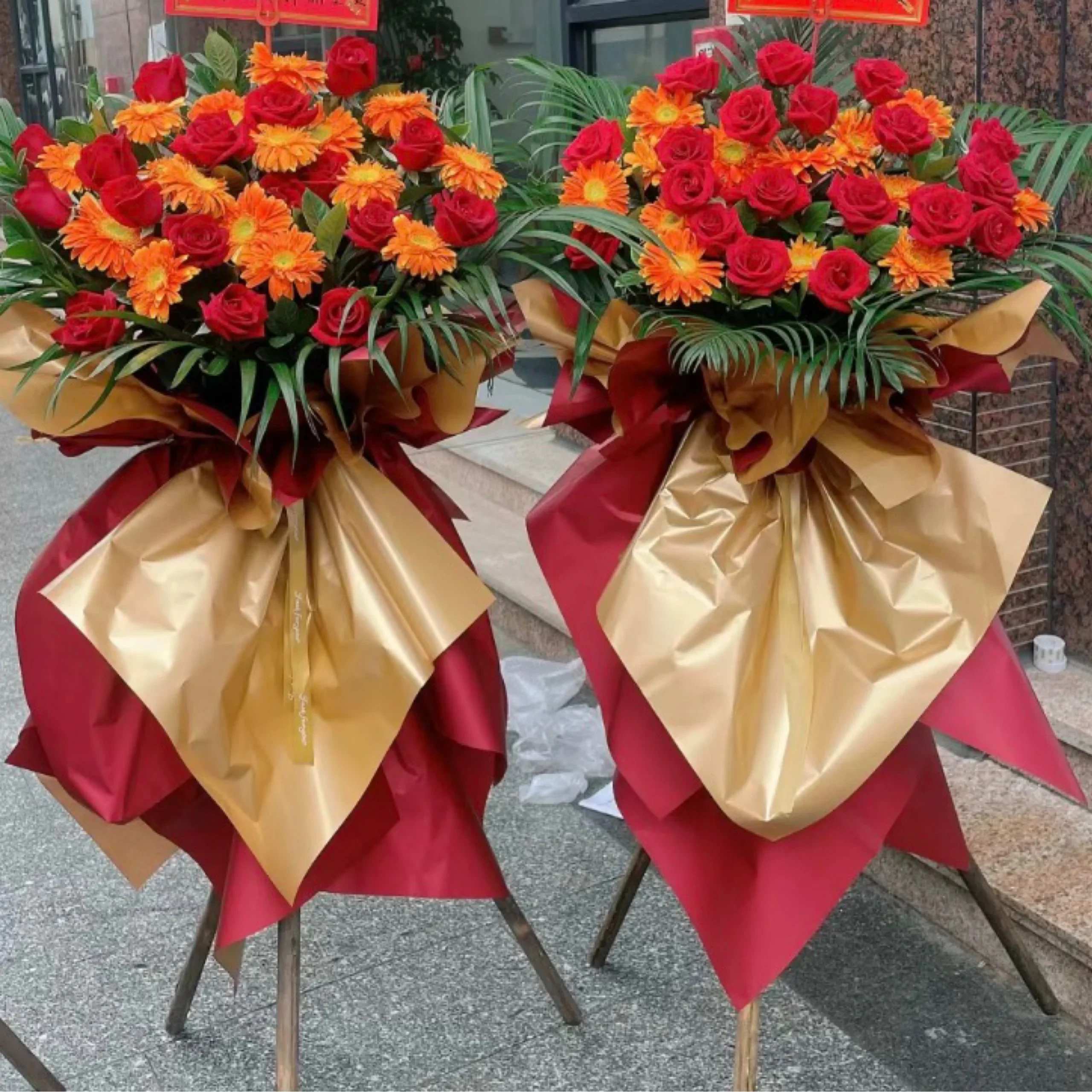 Two large bouquets of red roses and orange daisies wrapped in gold and red paper