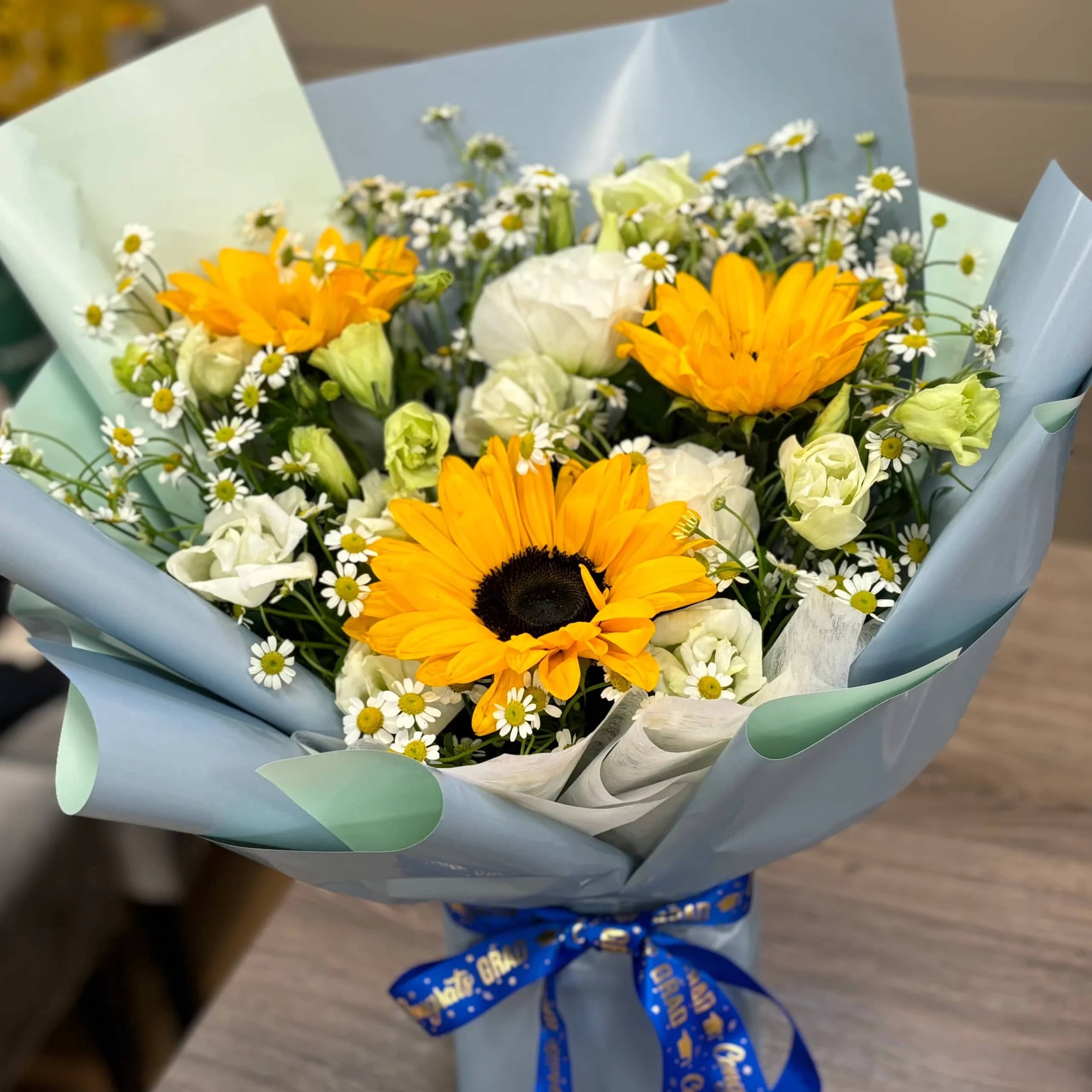 Bouquet of yellow sunflowers and white daisies wrapped in blue paper