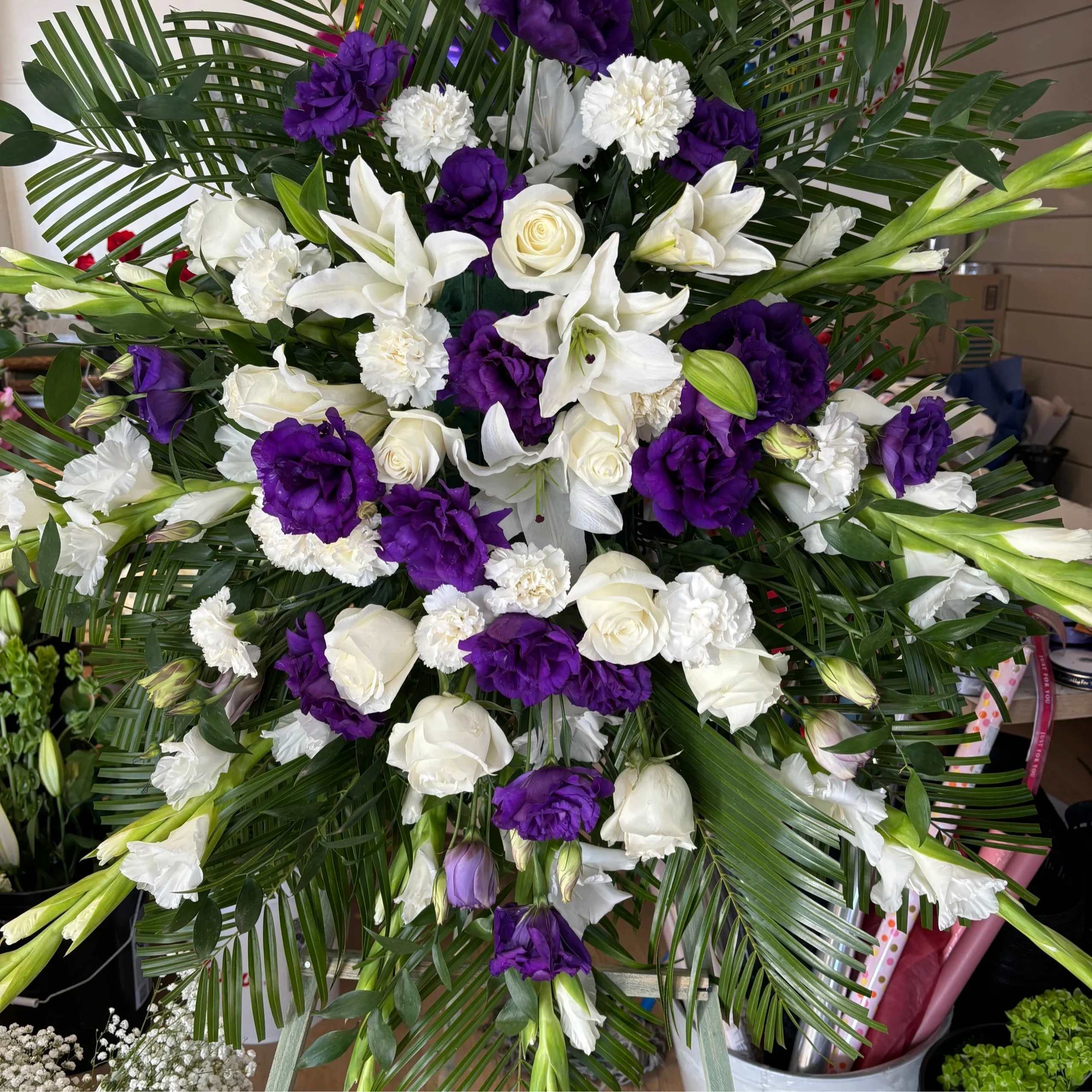 White lilies, roses, and purple blooms in a large standing spray