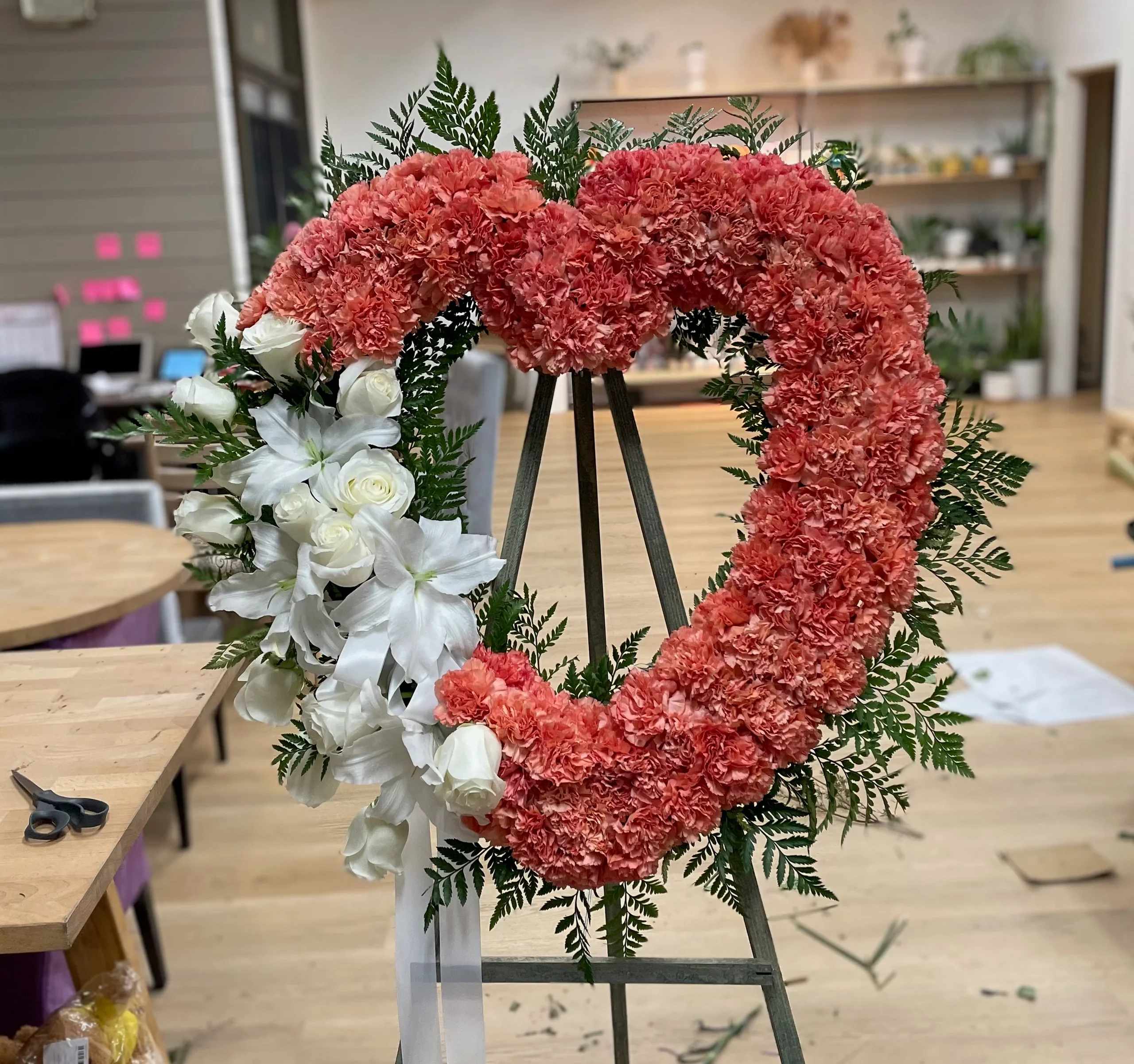 Heart-shaped floral wreath with pink carnations and white roses on an easel