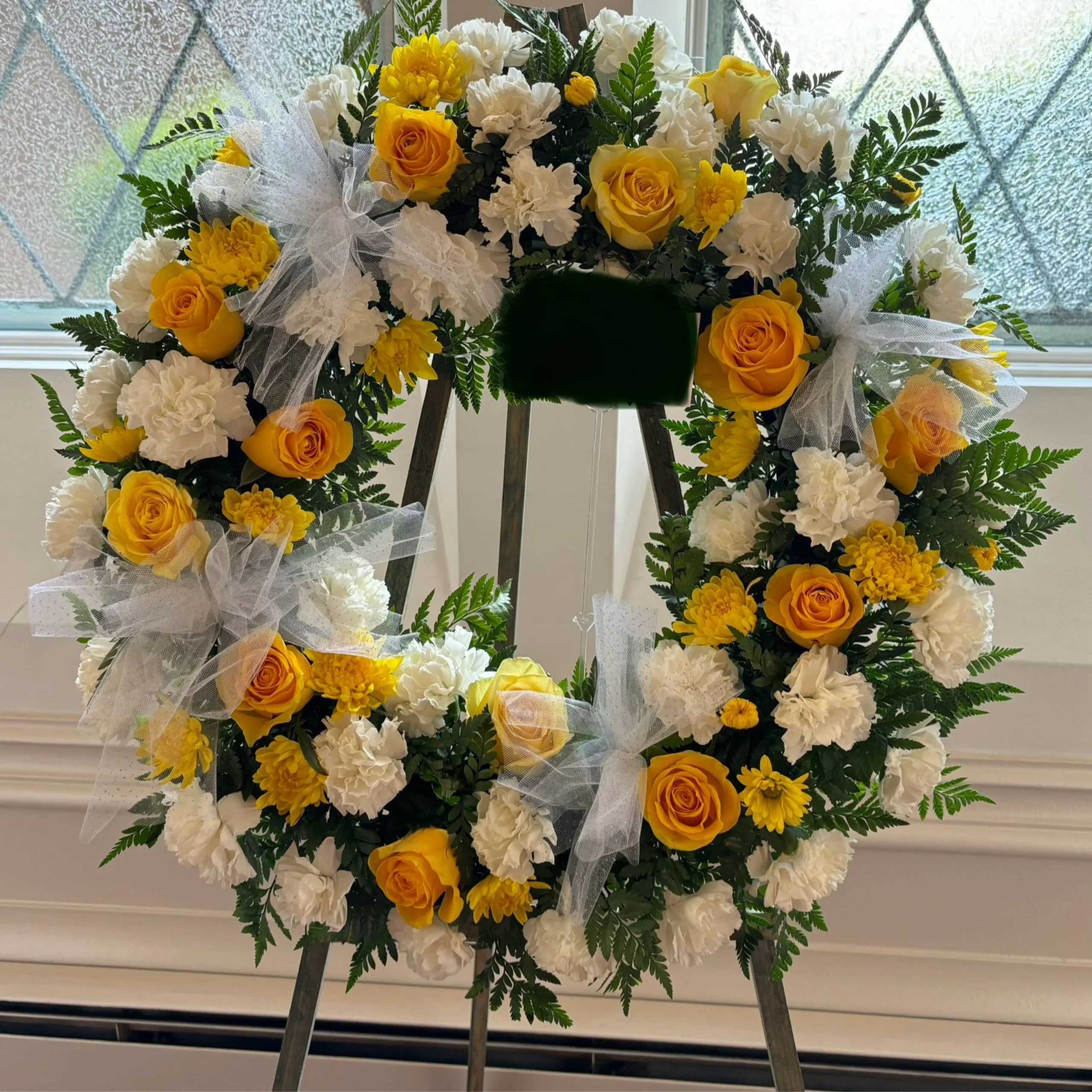 Yellow and white floral wreath with tulle bows on an easel