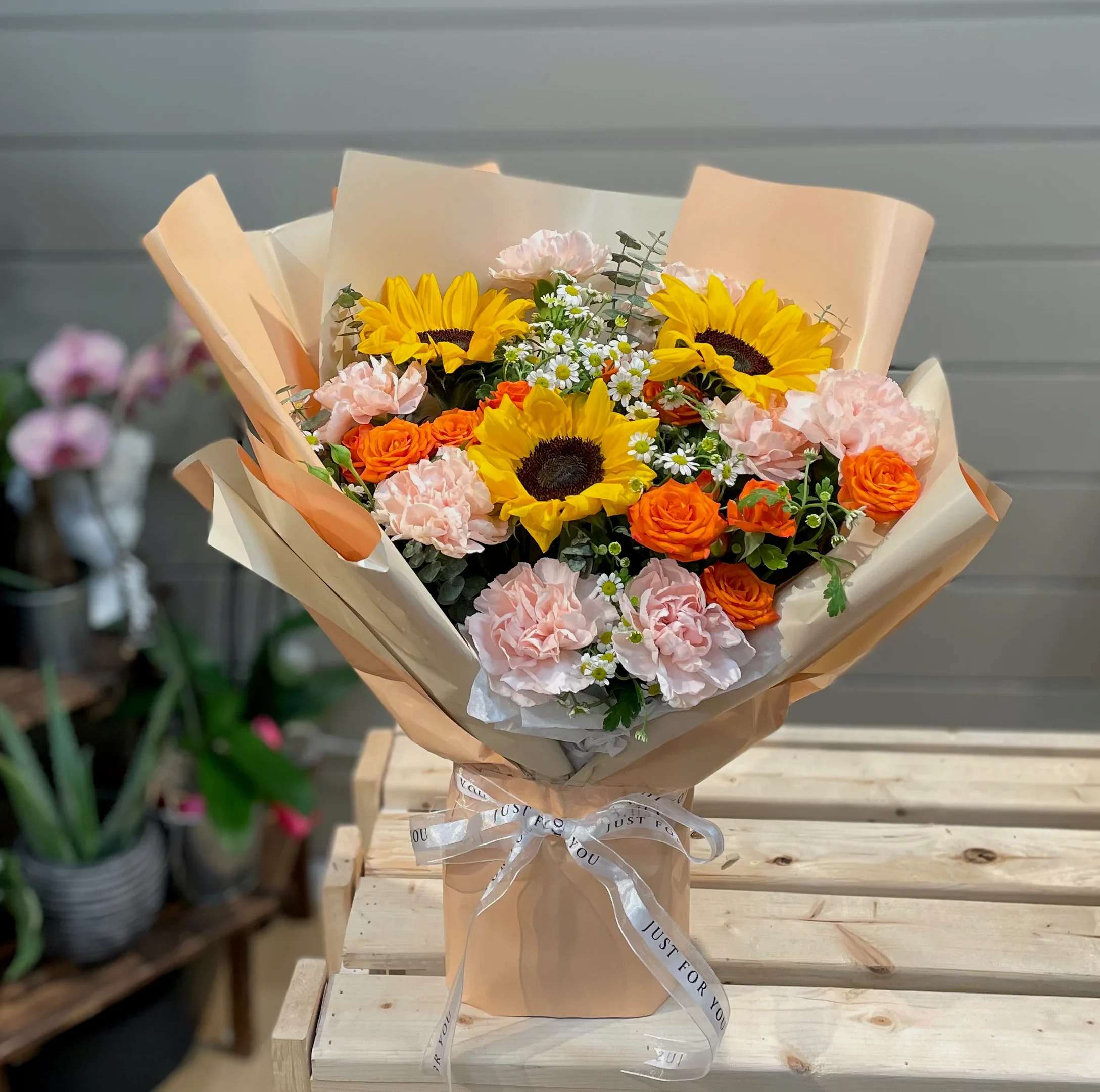Bouquet of sunflowers, orange roses, and pale pink carnations wrapped in tan paper