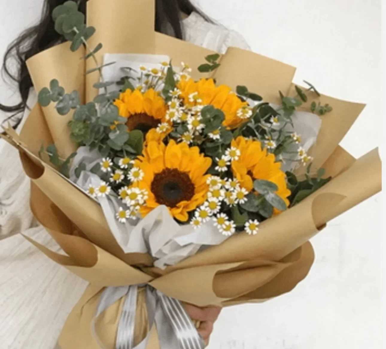 Bouquet of sunflowers and small white daisies wrapped in brown paper