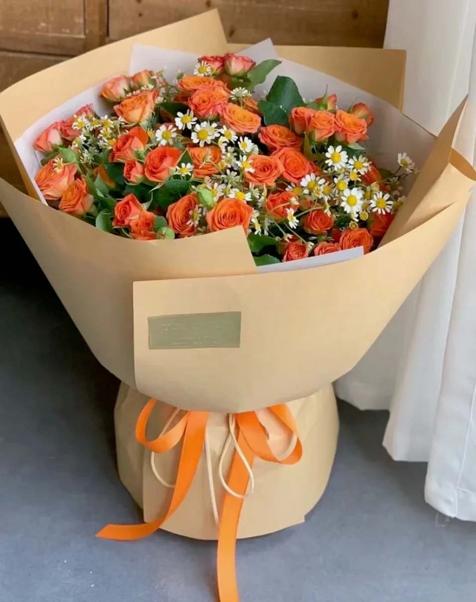 Bouquet of orange roses and white daisies wrapped in tan paper