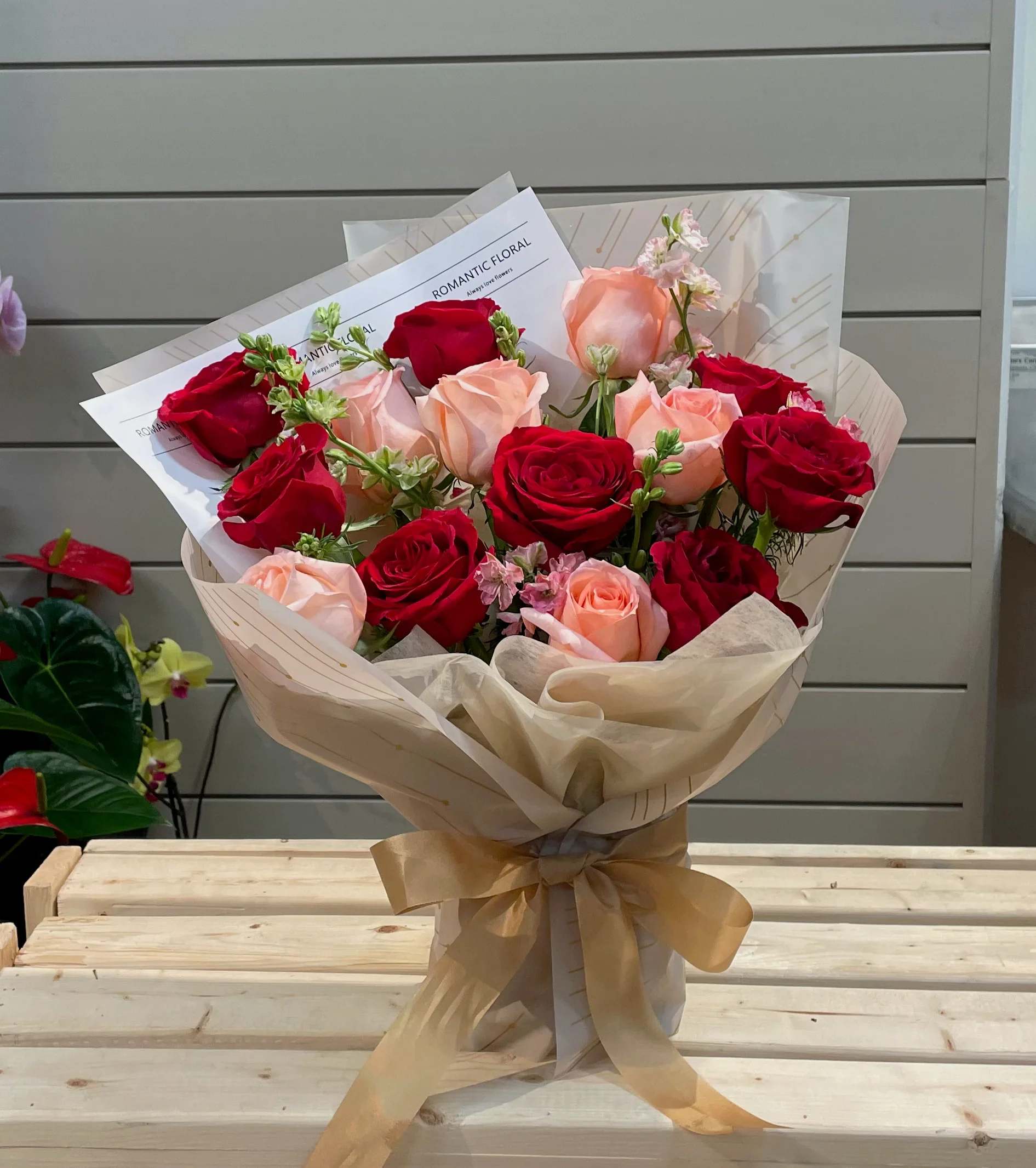 Bouquet of red and blush roses wrapped in cream paper with a gold ribbon