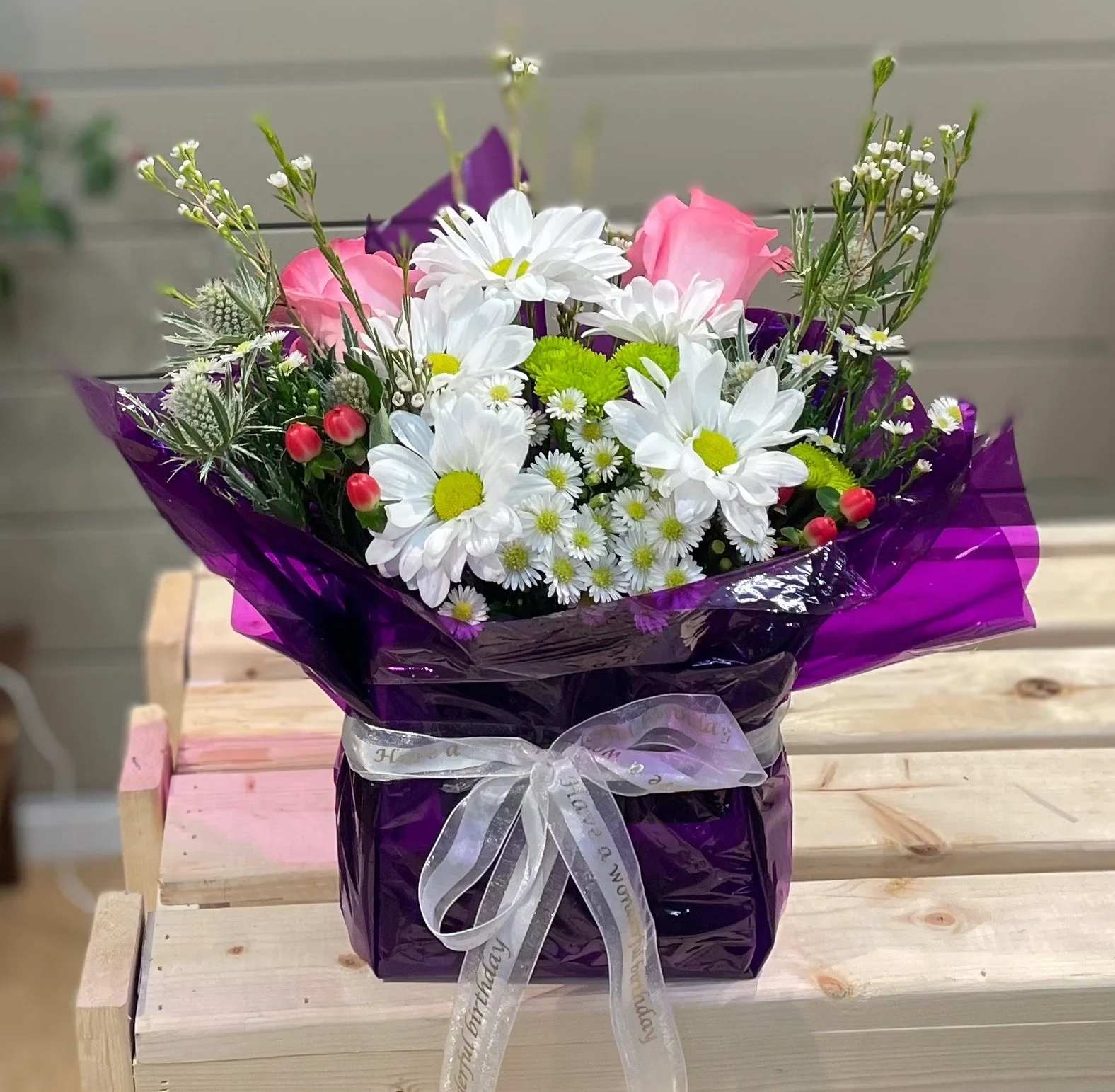 Bouquet of white daisies and pink roses wrapped in purple paper