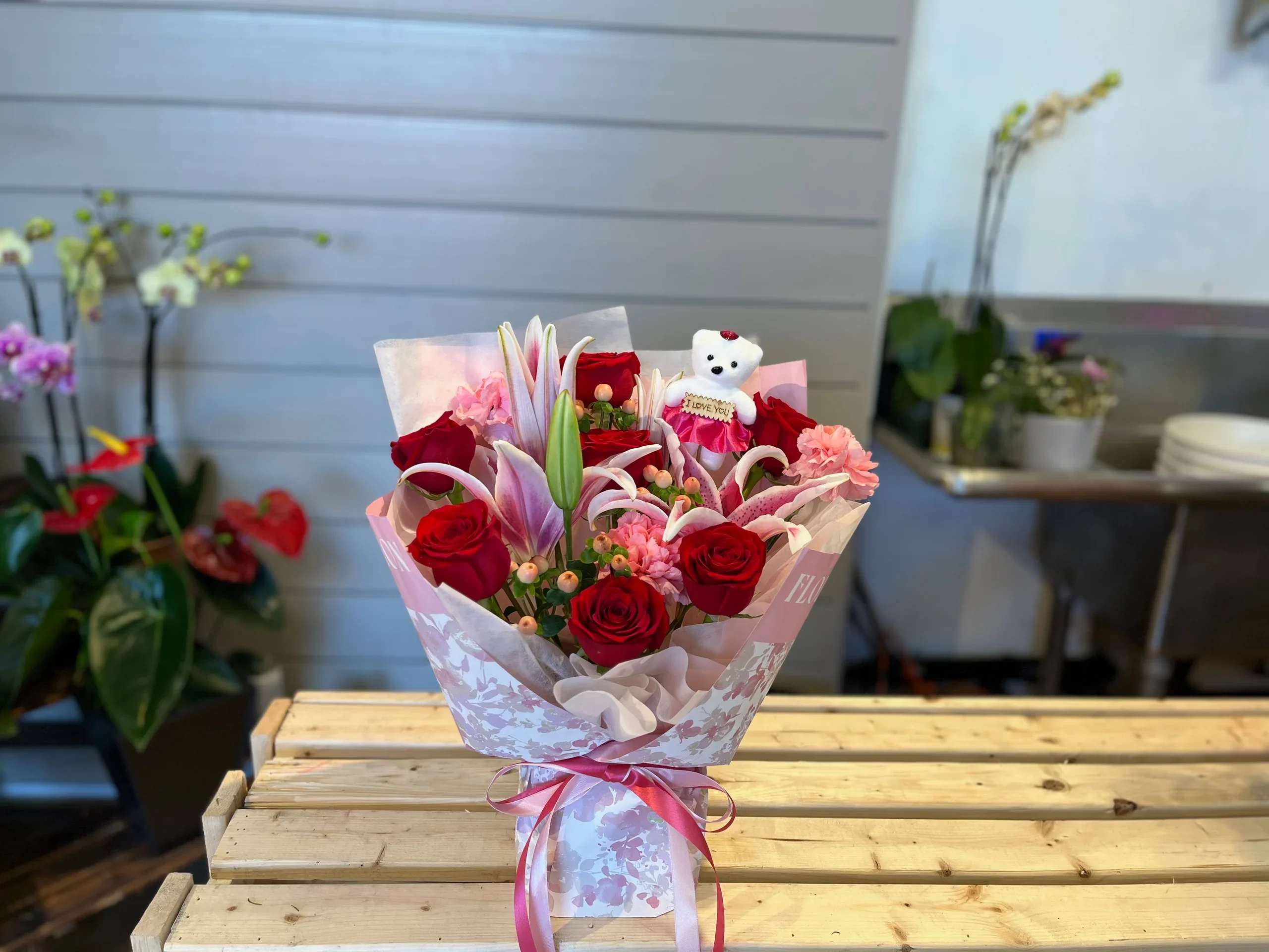 Bouquet of red roses and pink lilies with a small teddy bear