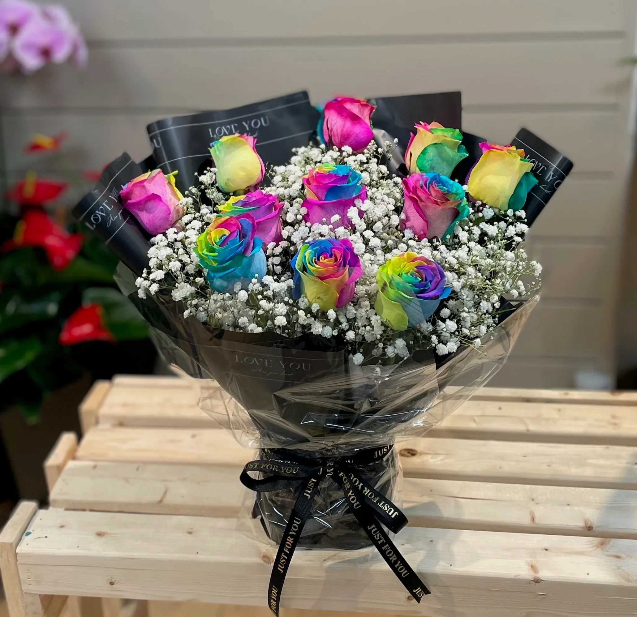 Bouquet of rainbow-colored roses with baby's breath in black wrapping