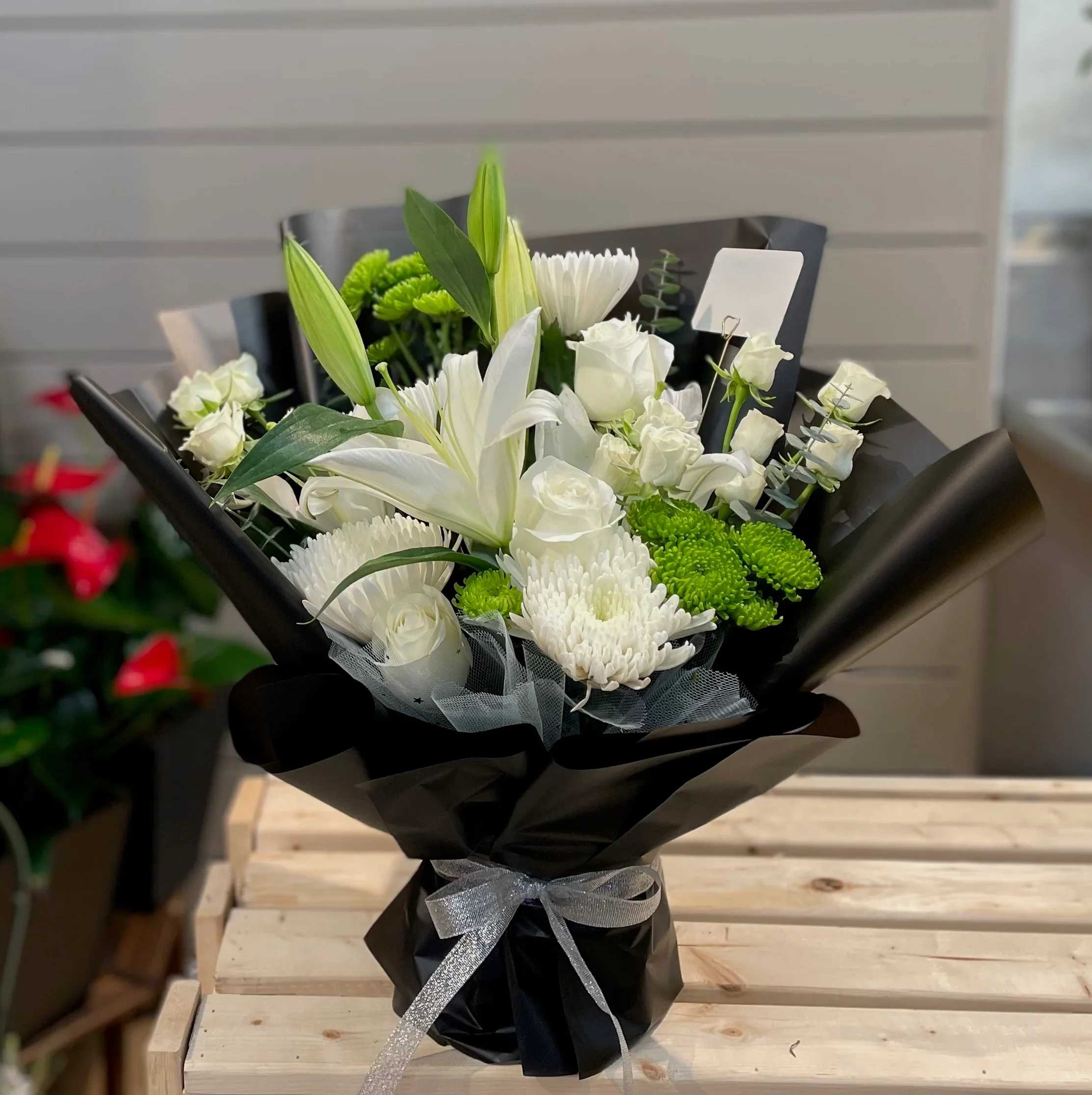 White lilies and roses arranged with green mums in black wrap