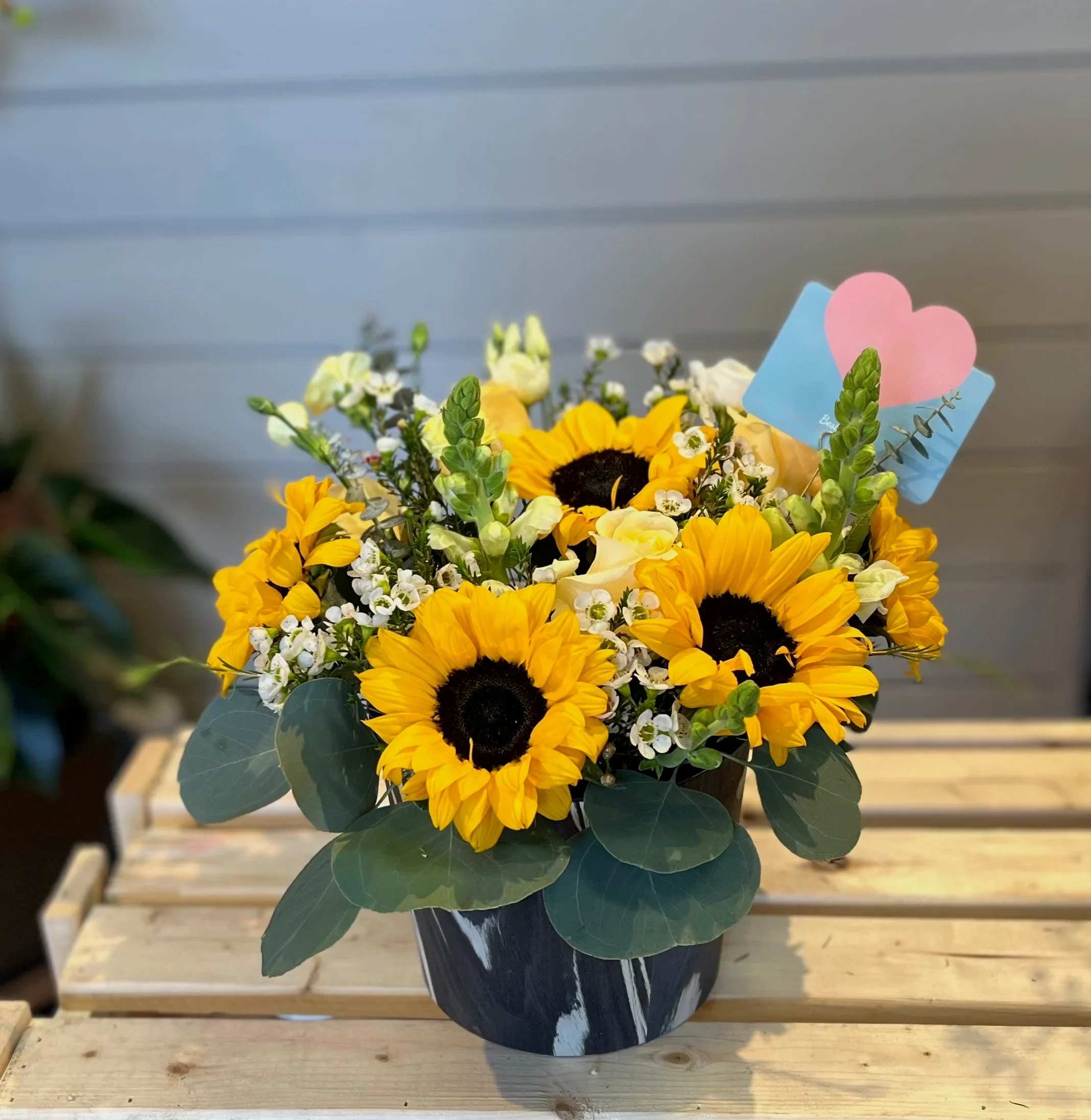 Sunflower bouquet in a dark vase with a pink heart pick