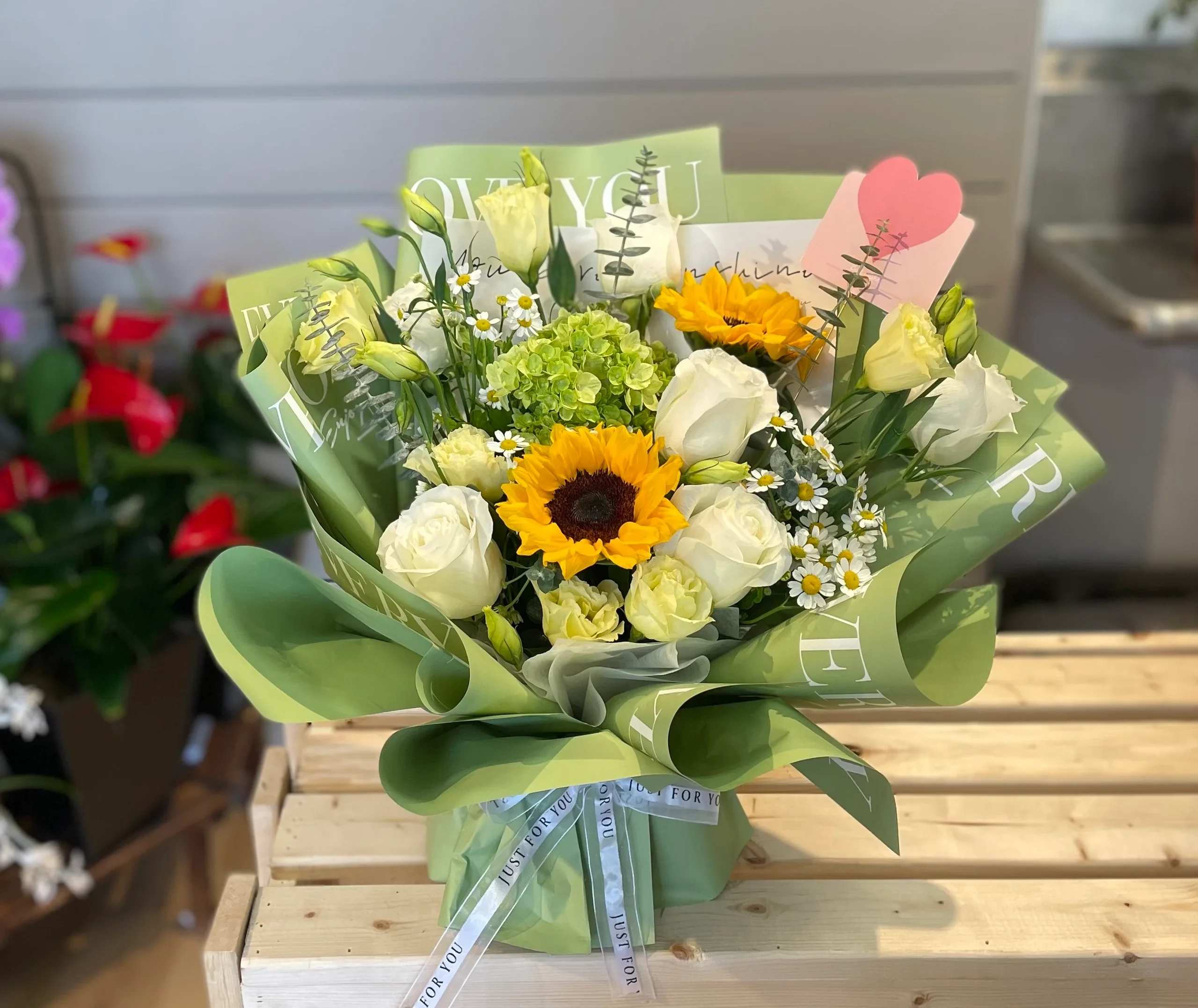 Bouquet of white roses, sunflowers, and small daisies wrapped in green paper