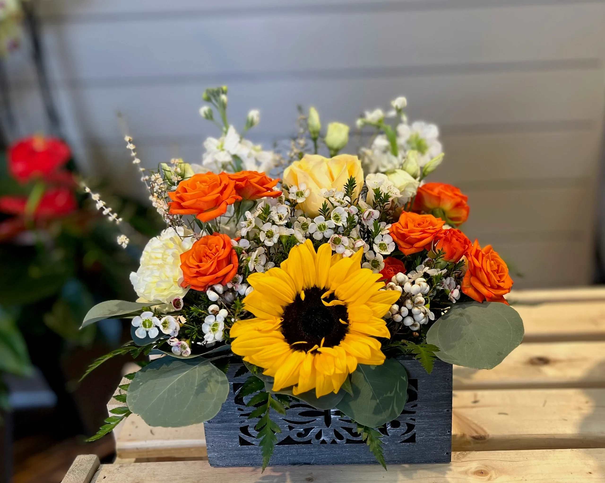 Orange roses and a yellow sunflower in a dark wooden box