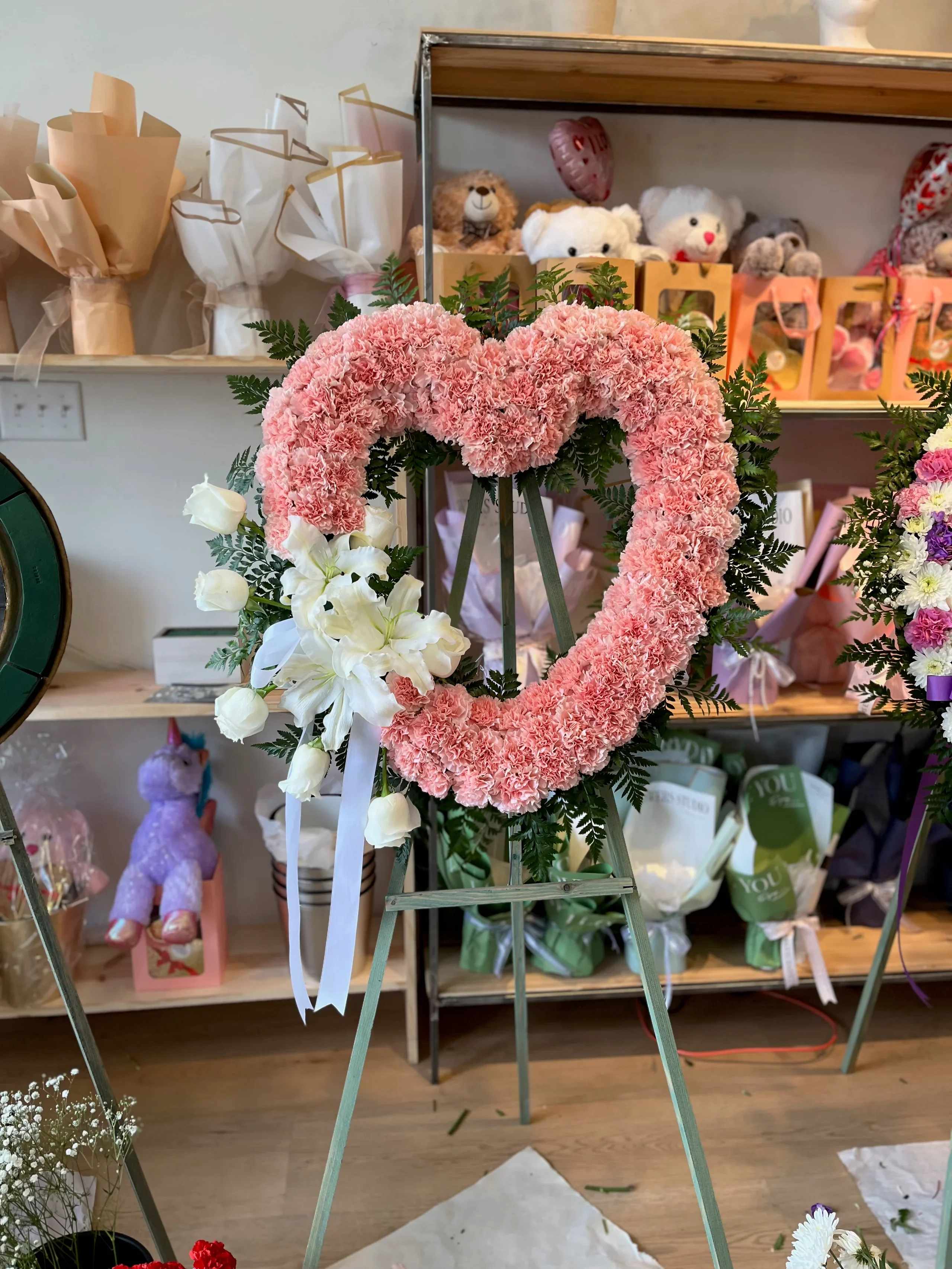 Pink carnation heart wreath on an easel with white lilies and ribbon