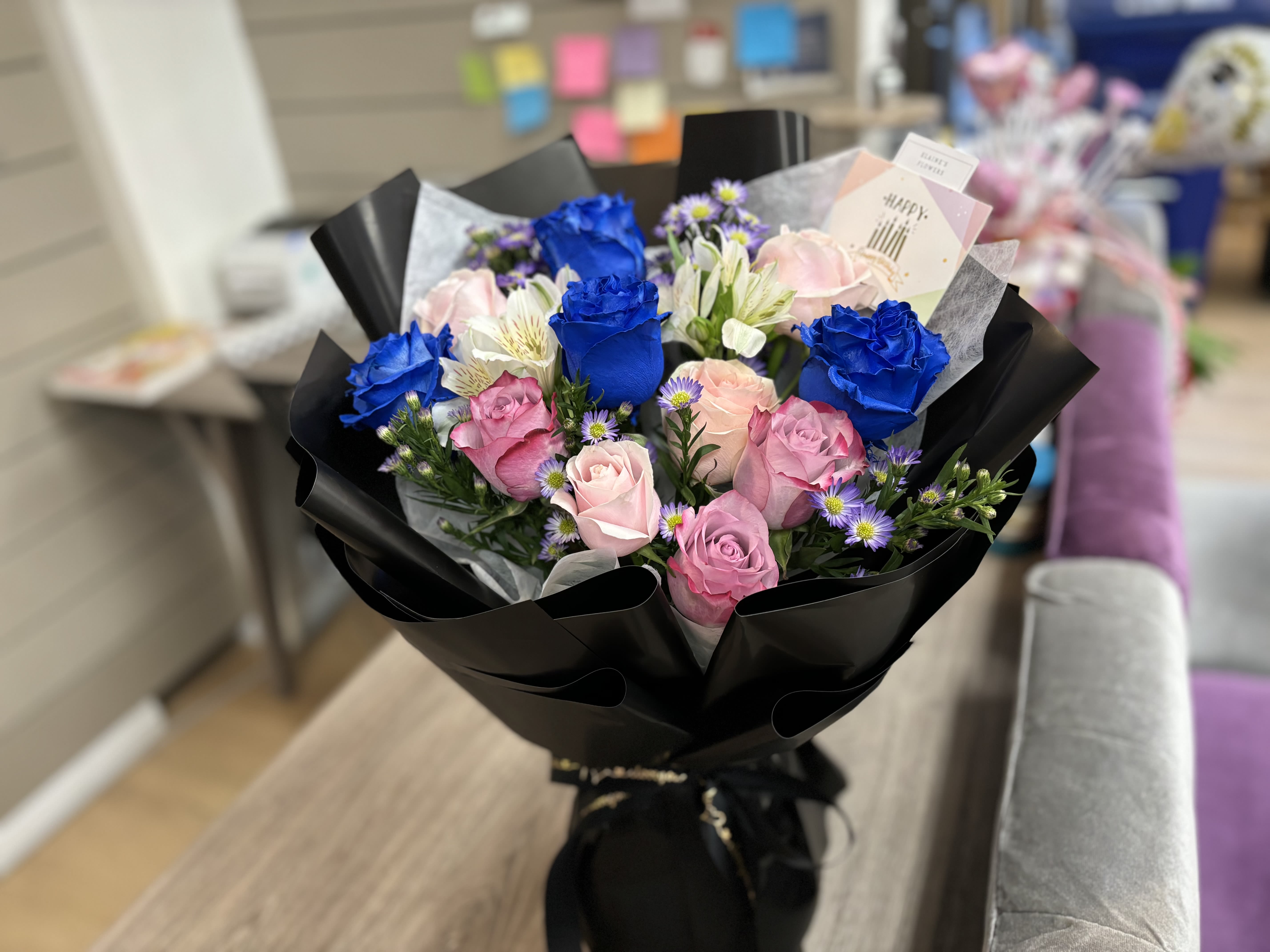 Bouquet of blue and pink roses with small purple flowers in black wrap