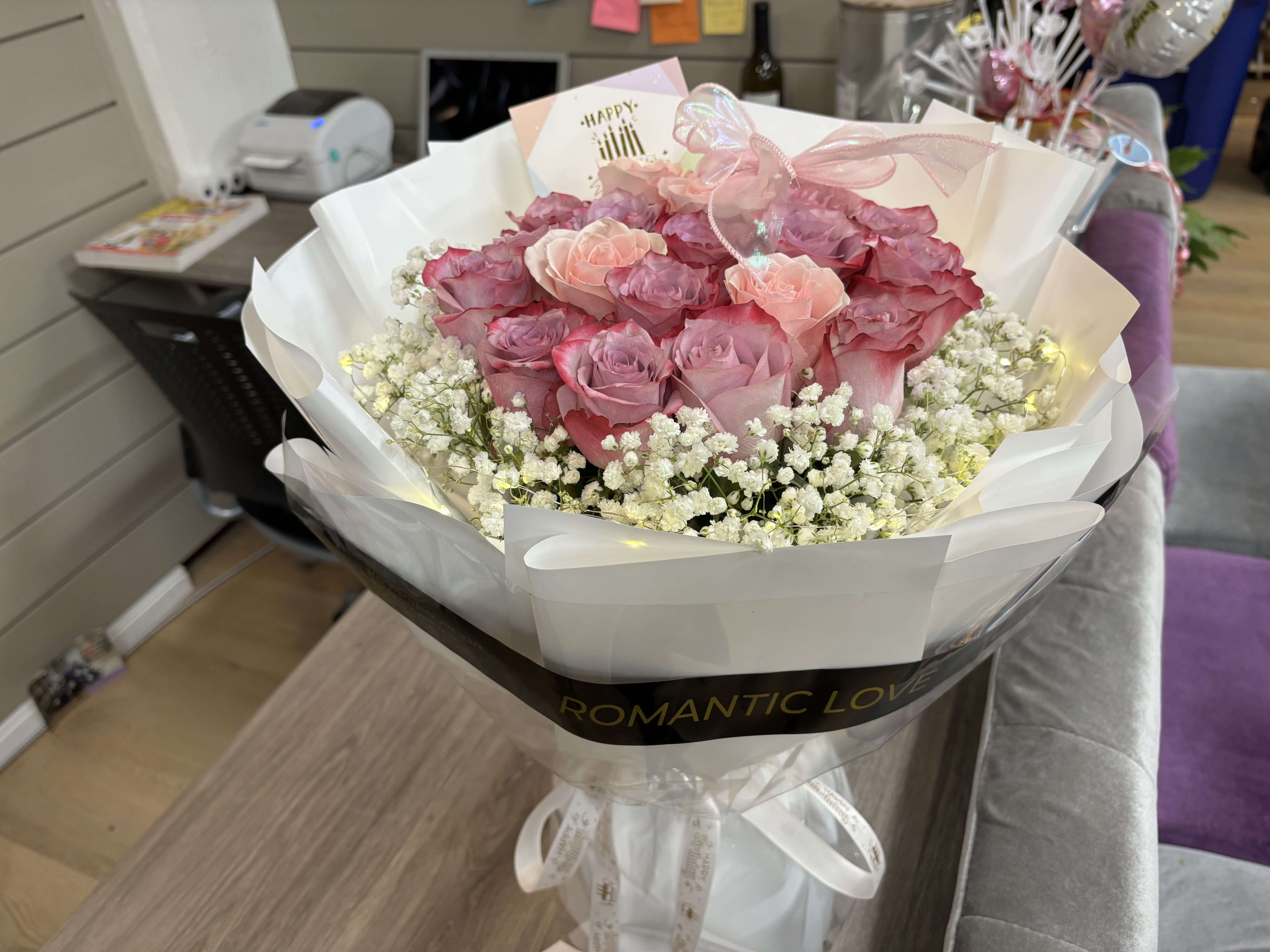 Pink roses wrapped in white paper with baby's breath and a ribbon