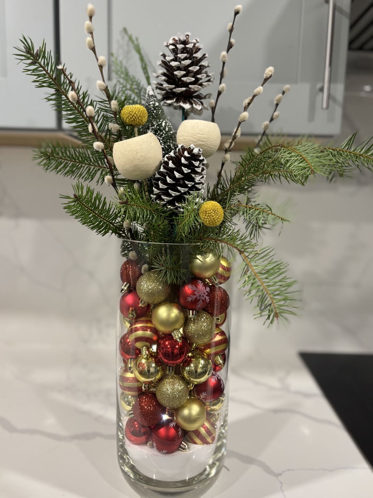 Holiday arrangement in a glass vase with pinecones and red-gold ornaments