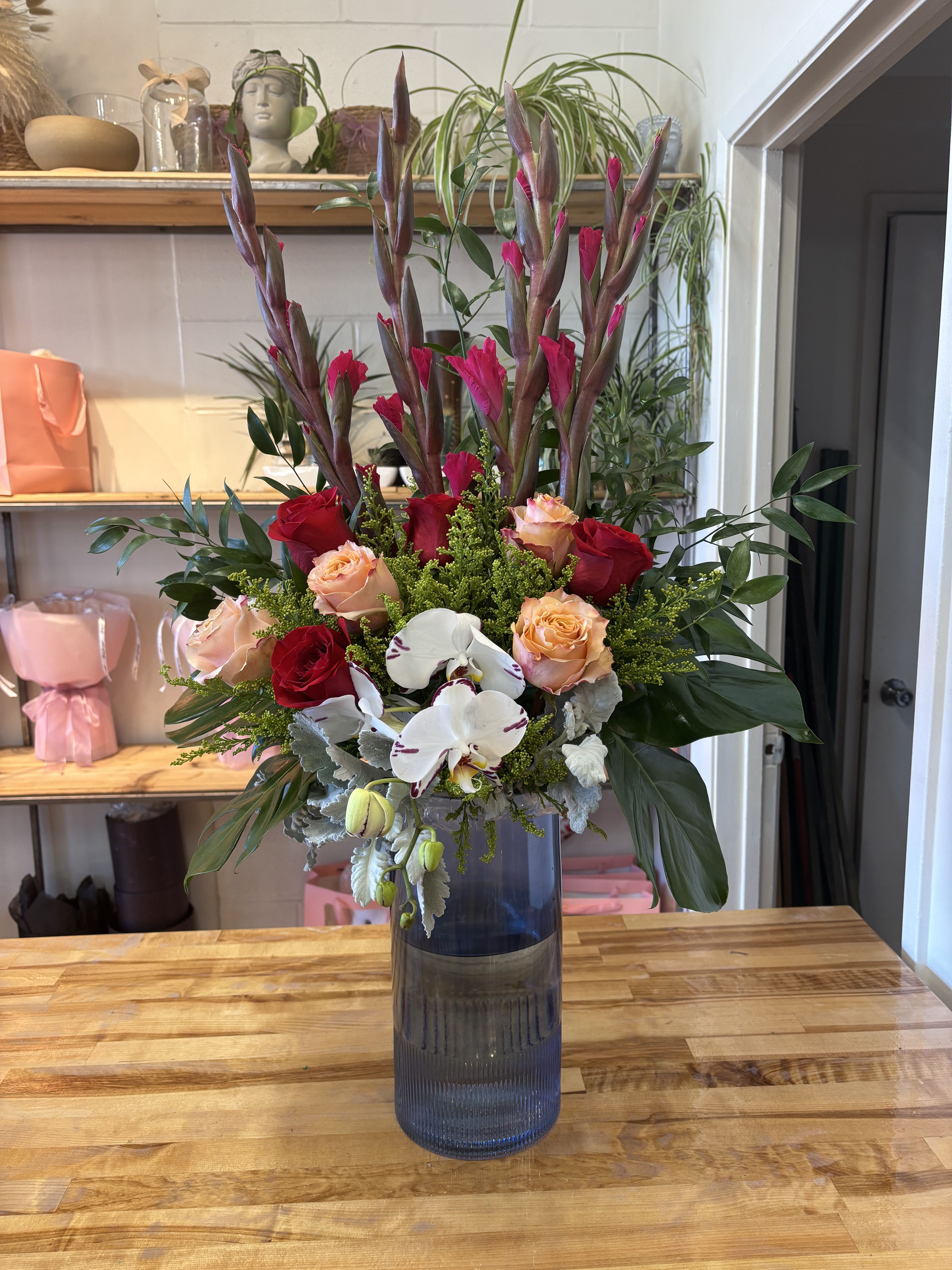 Tall bouquet of red and peach roses with white orchids in a blue vase