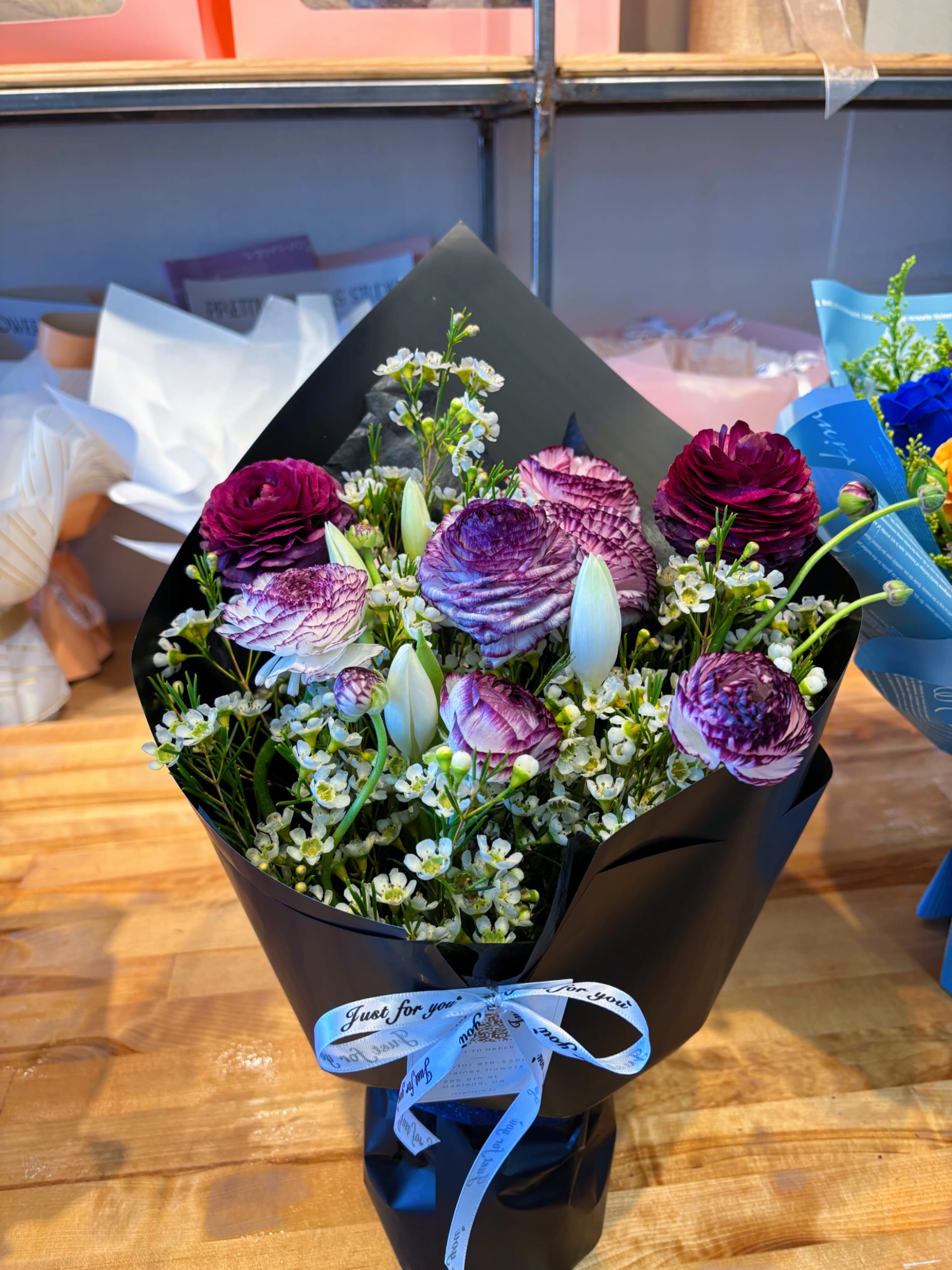 Bouquet of purple ranunculus and white accent flowers wrapped in black paper