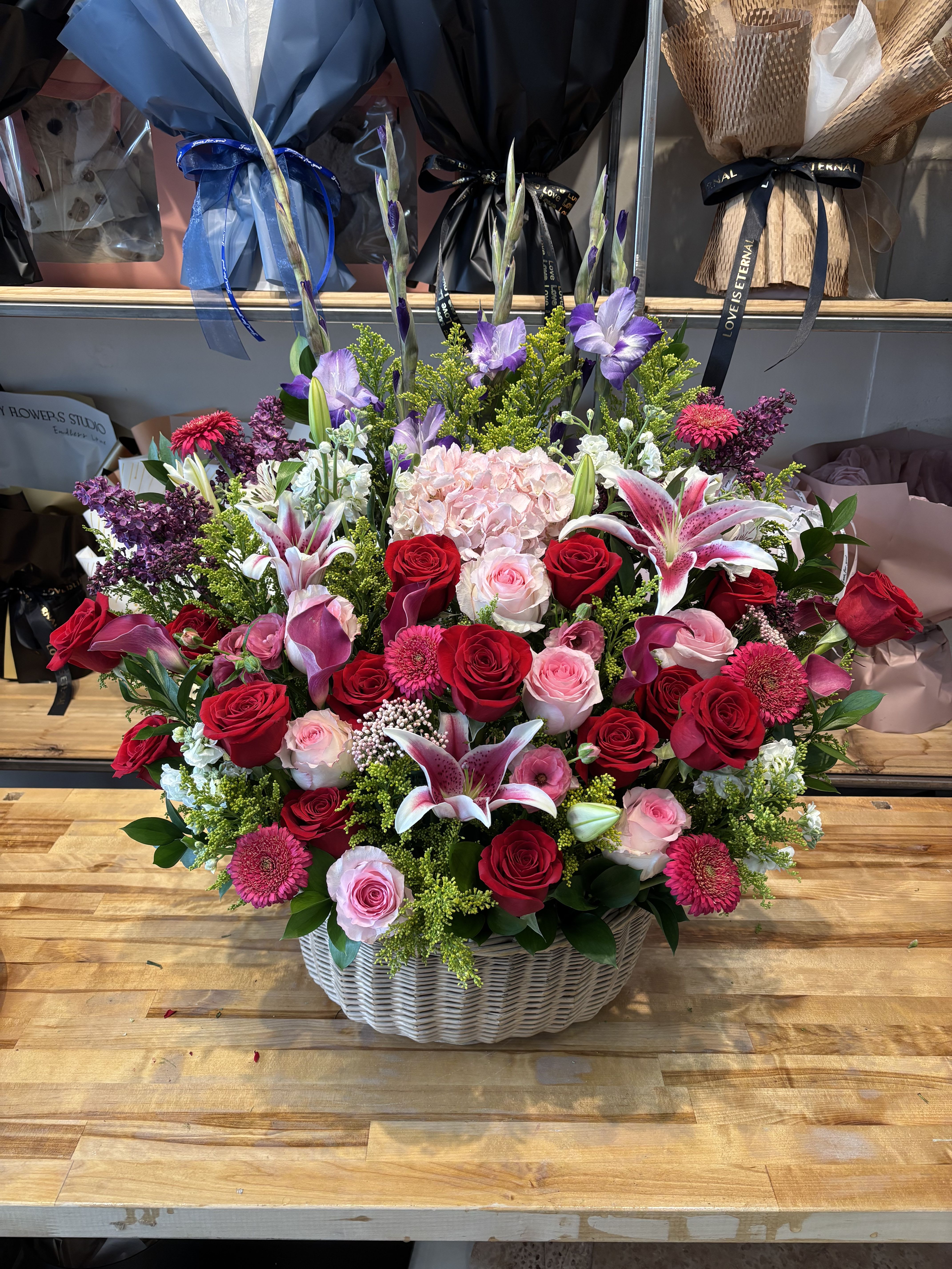 Large basket arrangement of red and pink roses with lilies and purple flowers