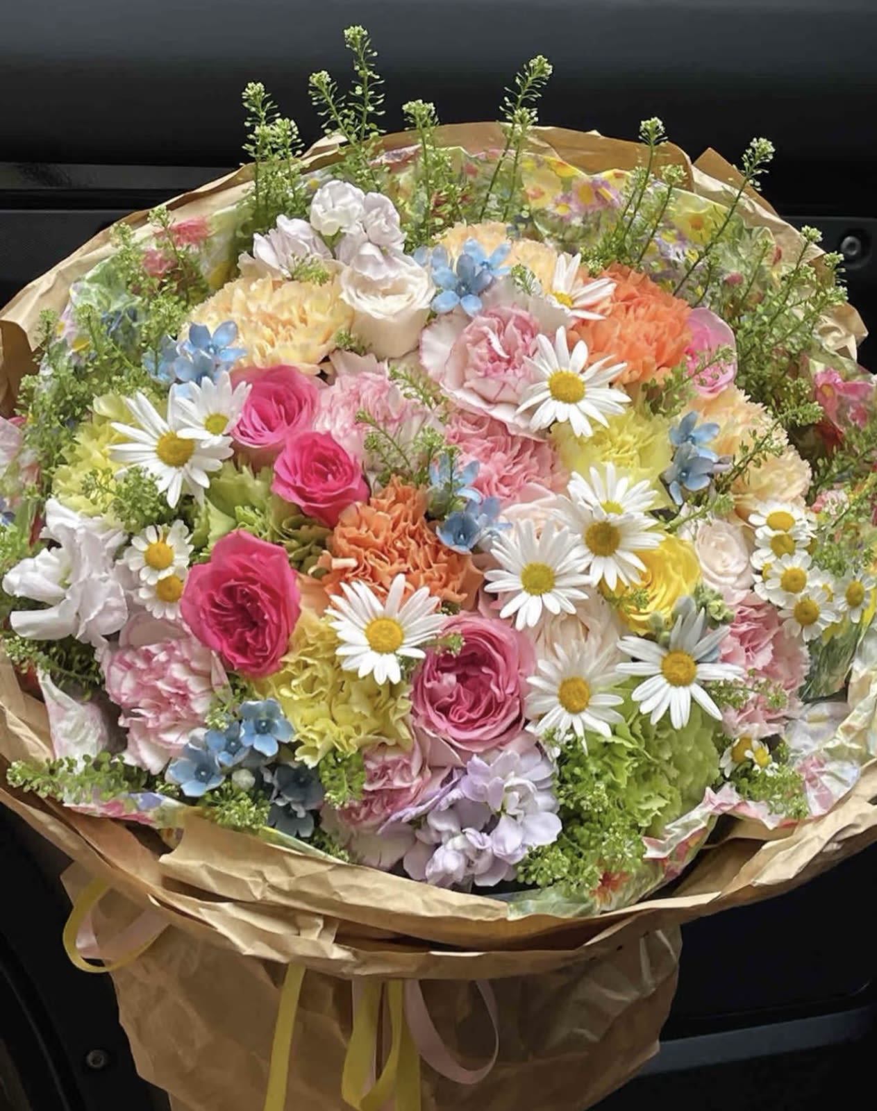 Mixed bouquet of pastel flowers with daisies and roses wrapped in brown paper