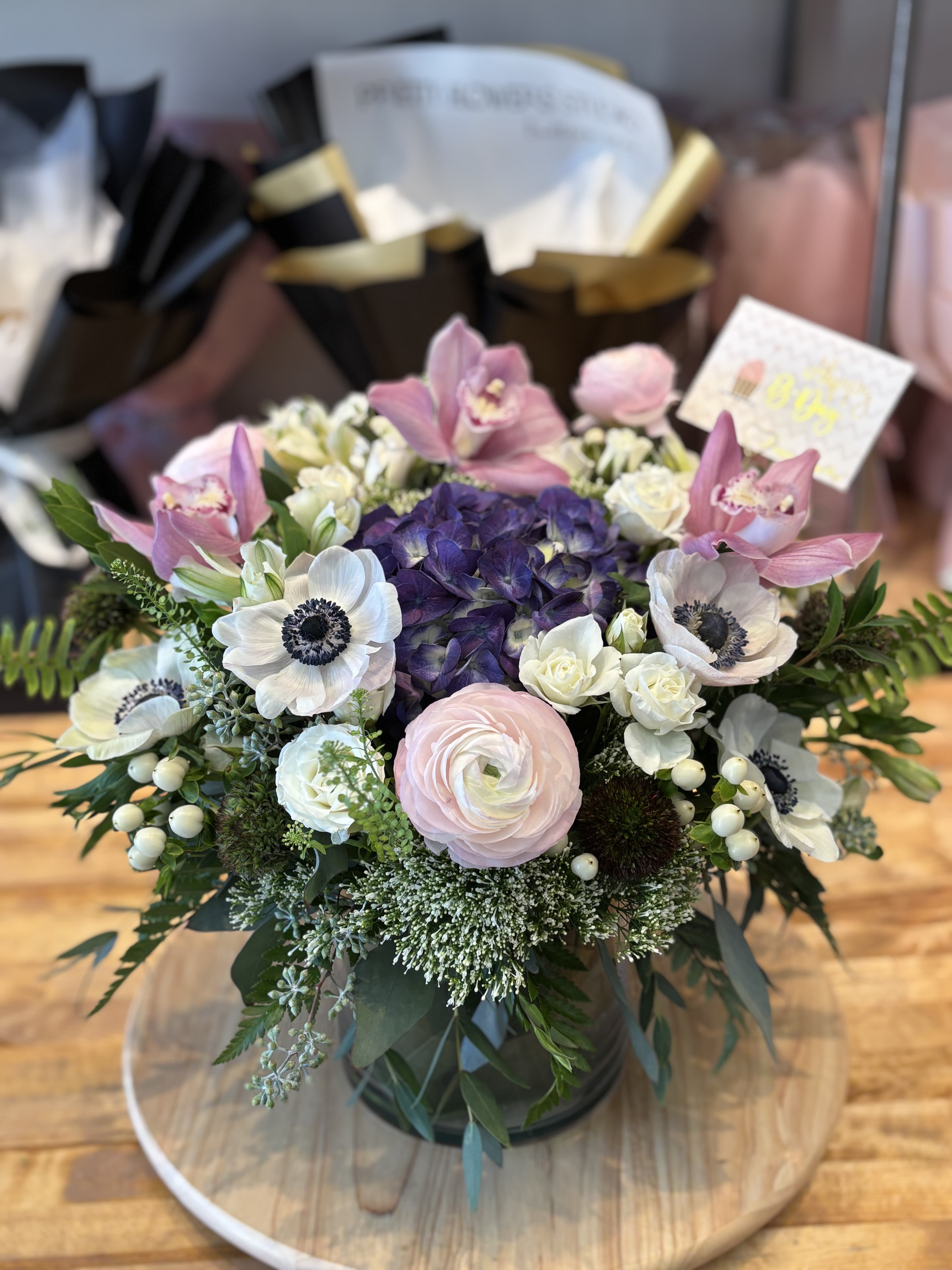 Round bouquet with pink orchids, white anemones, and purple hydrangea in a vase