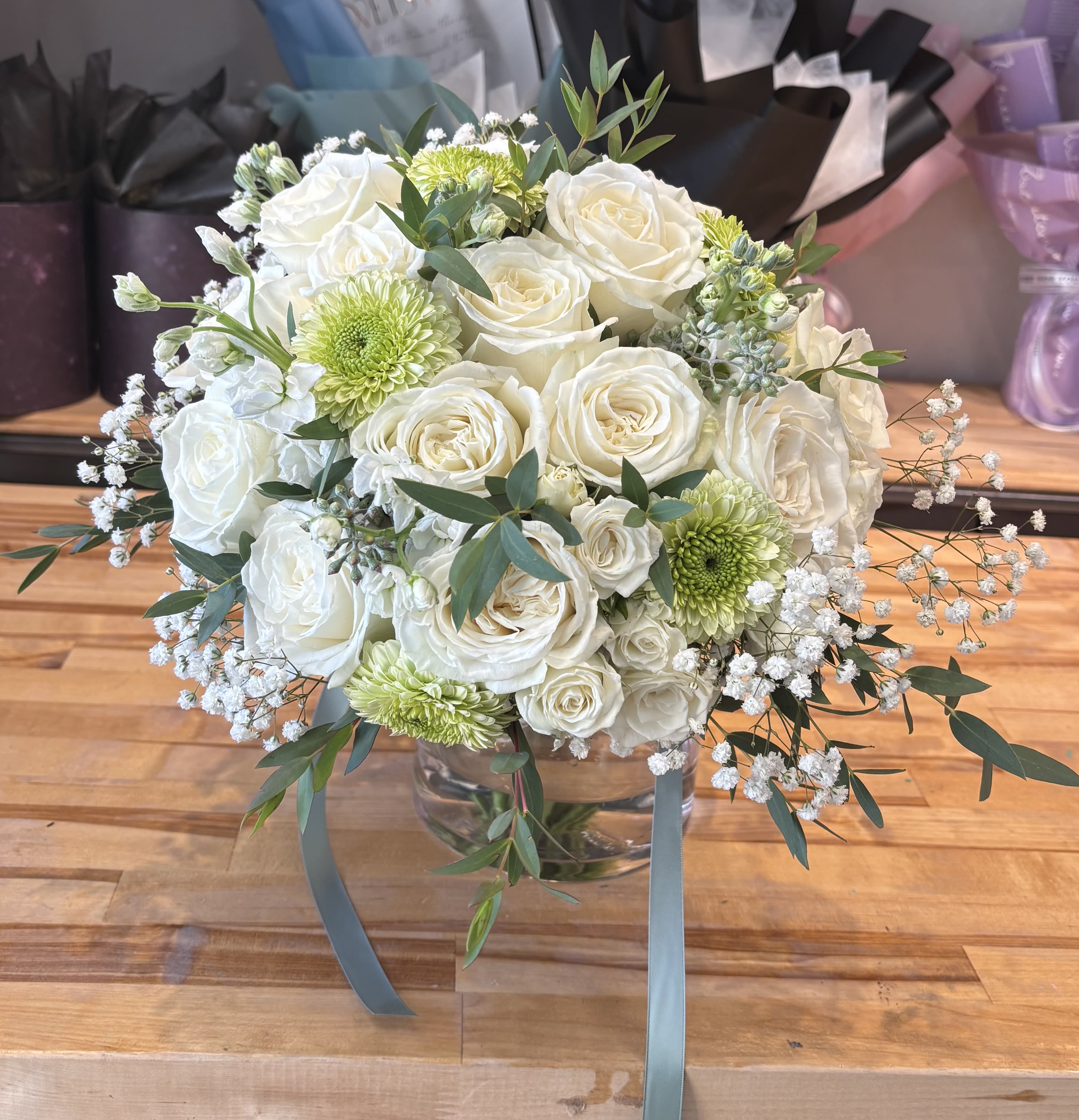 White roses and green chrysanthemums in a glass vase with trailing ribbon.