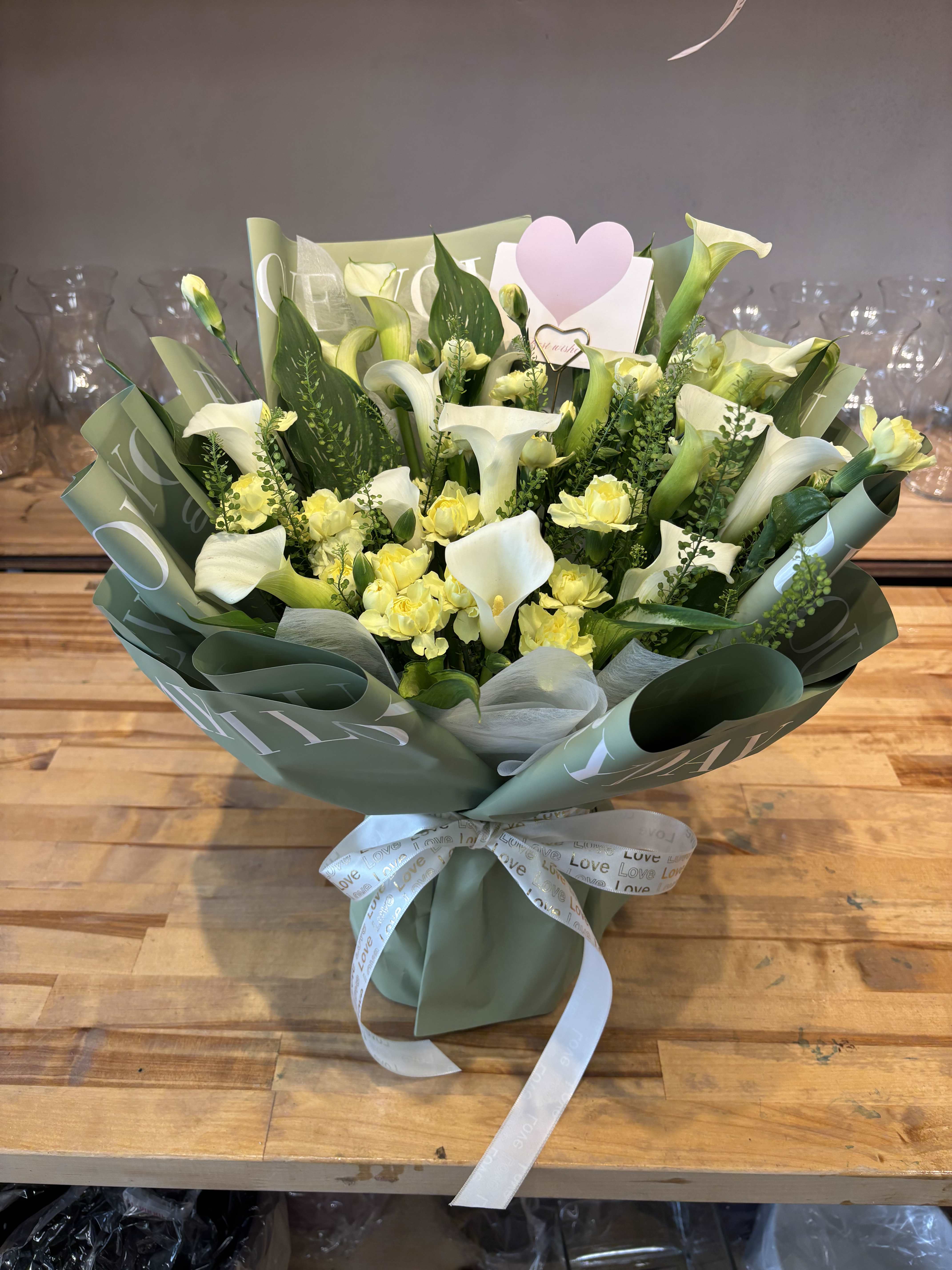 Bouquet of white calla lilies and yellow spray roses wrapped in green paper