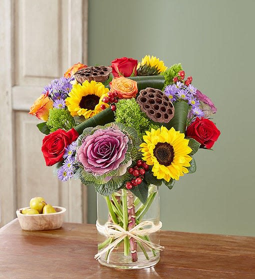 Majestic Garden - Fall - All-around arrangement with red roses and hypericum, autumn-colored roses, sunflowers, purple kale and monte casino; accented with assorted greenery and dried lotus pods. Arrangements are hand-designed so colors and varieties may be substituted with similar items based on local availability. 