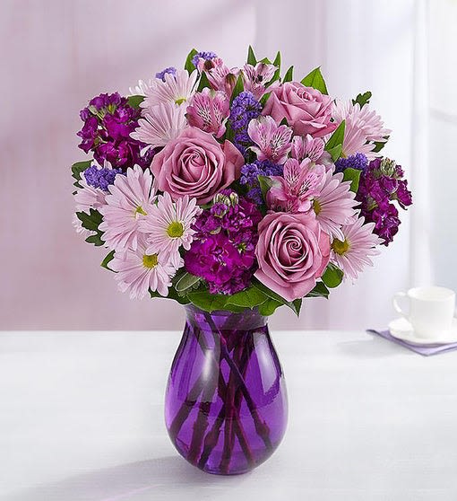 Lavender and purple mixed bouquet with roses and daisies in a purple glass vase