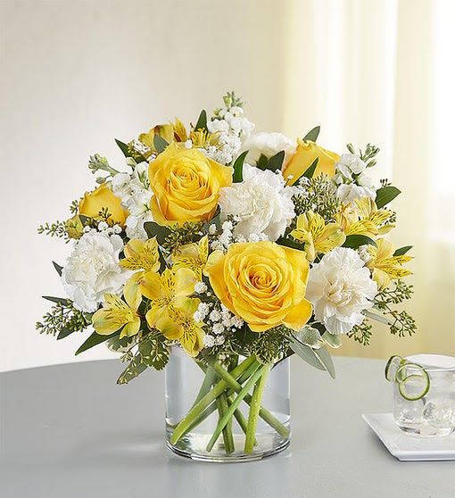 Yellow roses and white flowers arranged in a clear glass vase