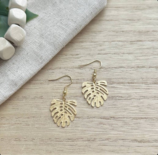 Pair of gold leaf-shaped dangle earrings on a wood surface