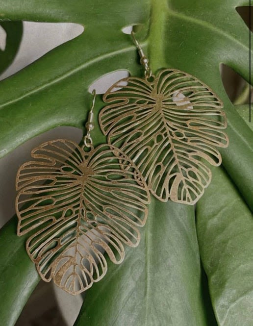 Pair of gold leaf-shaped dangle earrings on a green leaf background