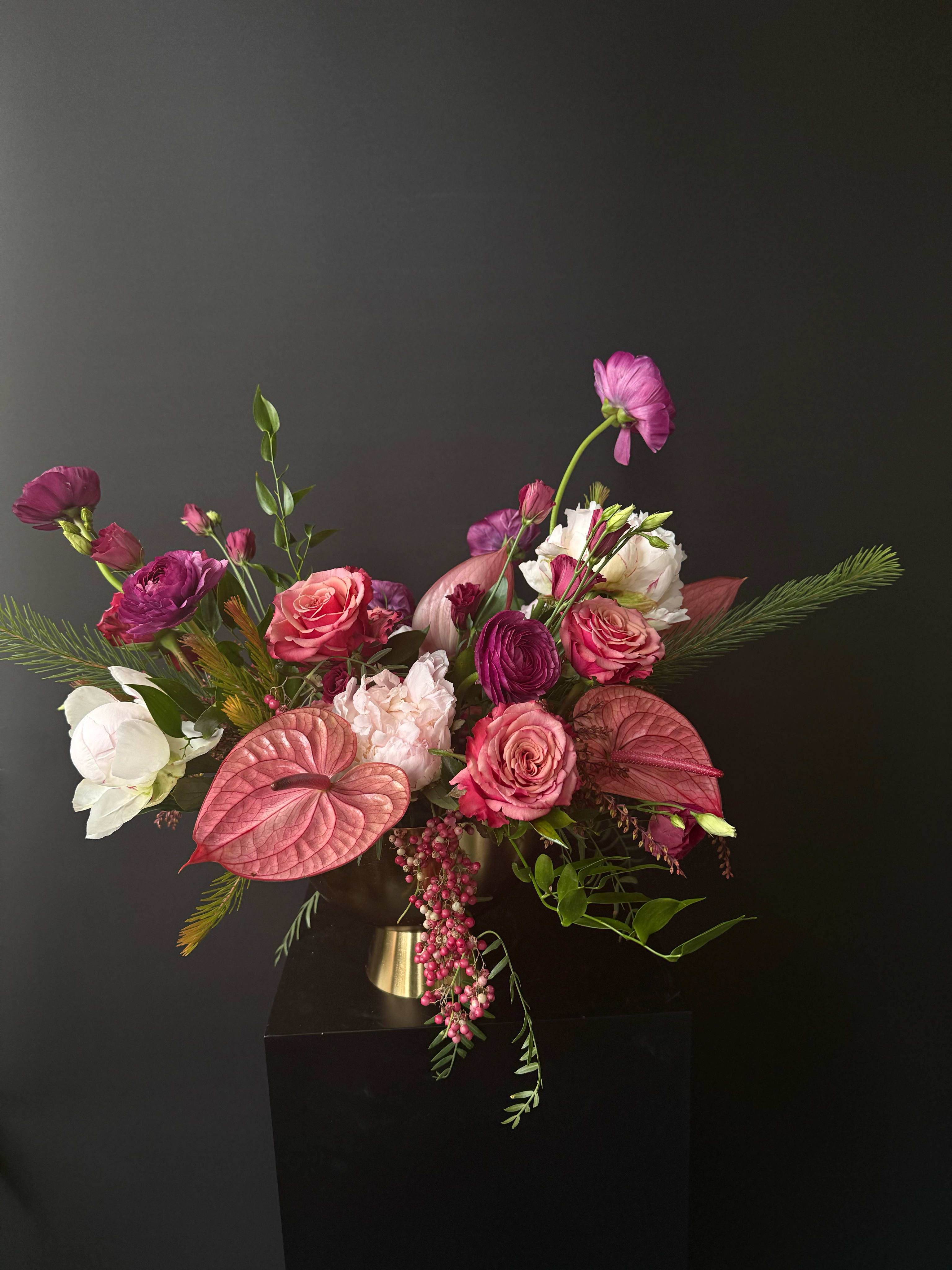 Asymmetrical arrangement of pink and purple flowers in a gold pedestal vase against a dark background