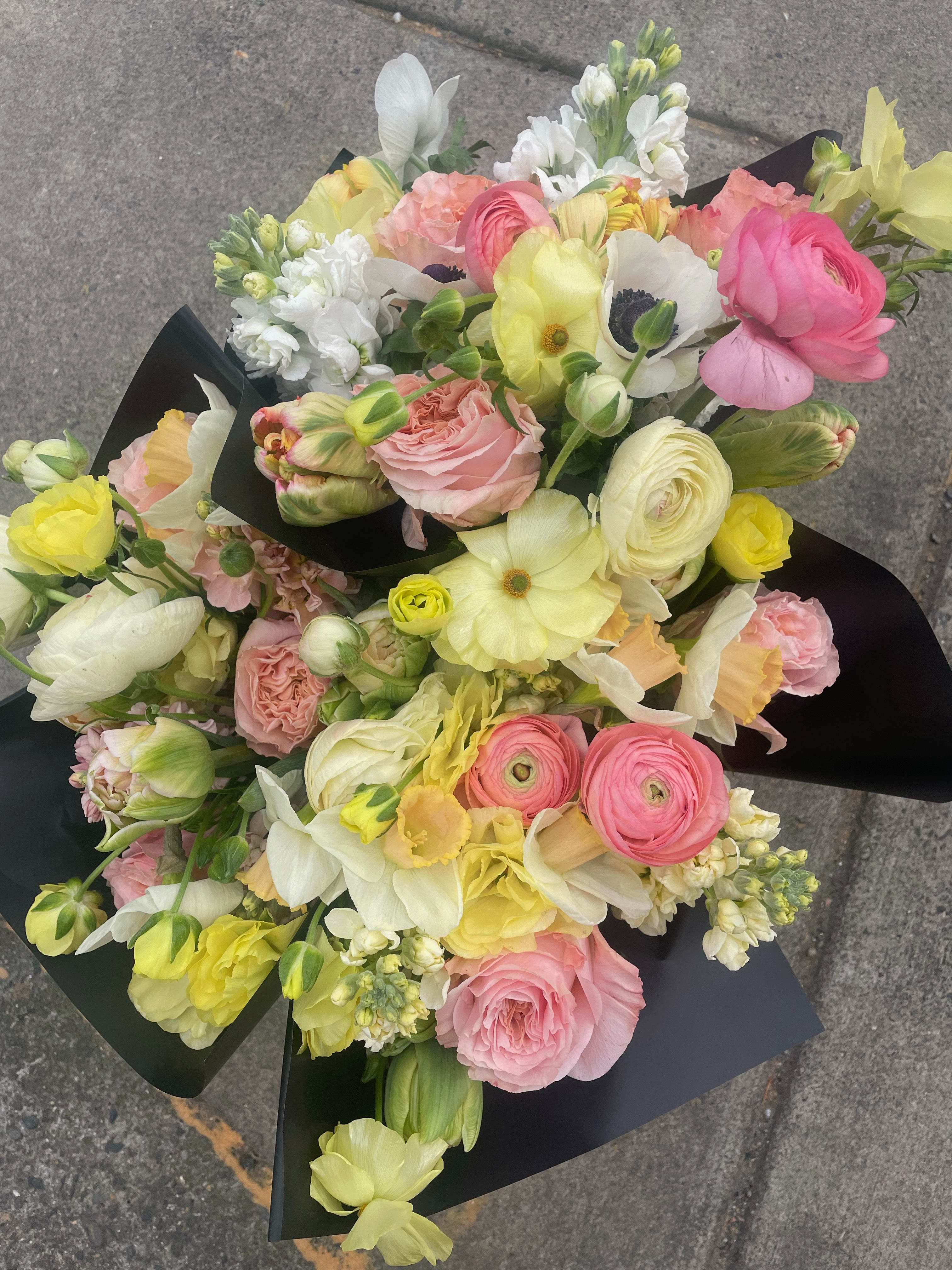 Mixed bouquet of pink, yellow, and white flowers wrapped in black paper