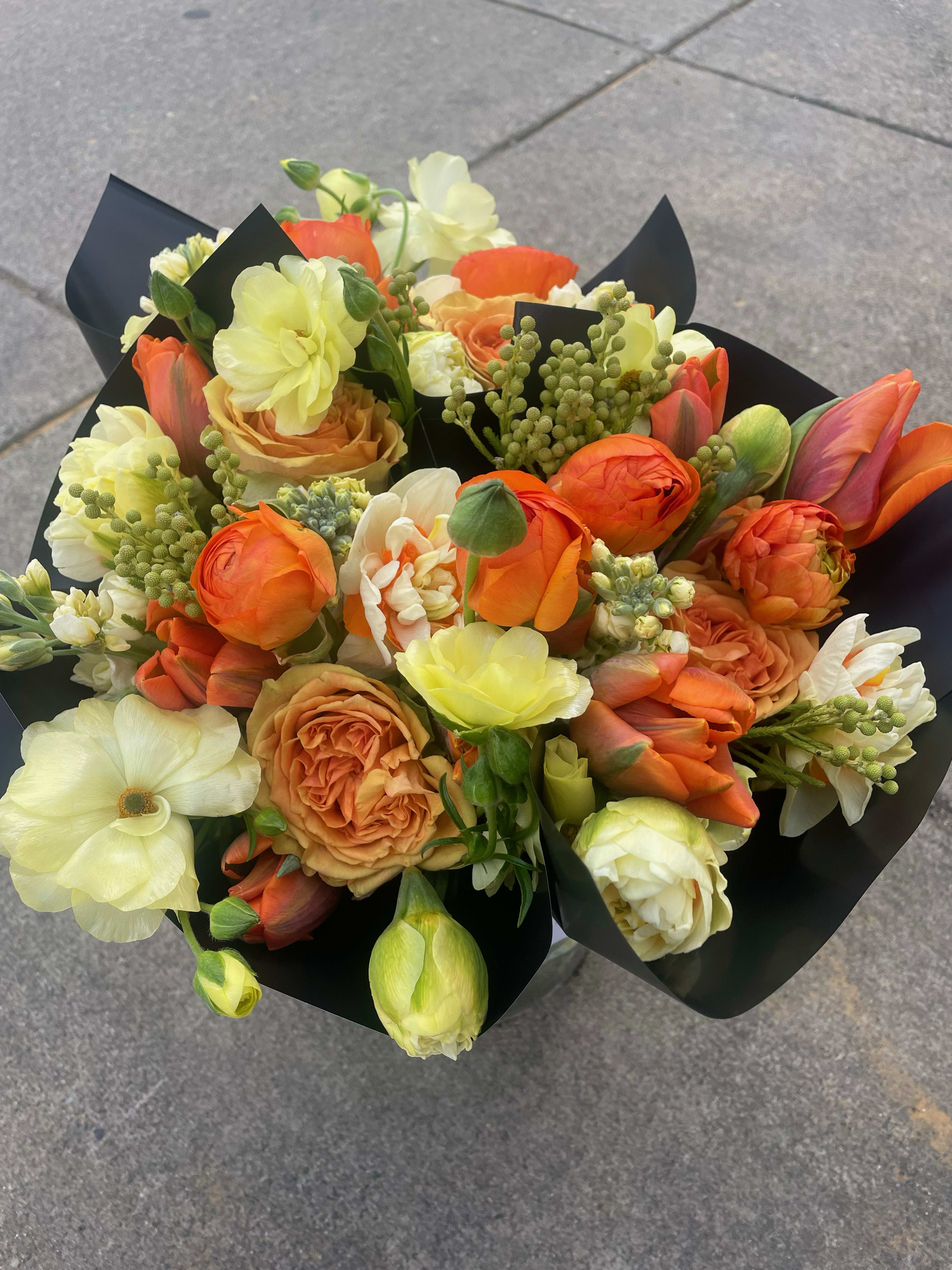 Bouquet of orange, cream, and pale yellow flowers wrapped in black paper