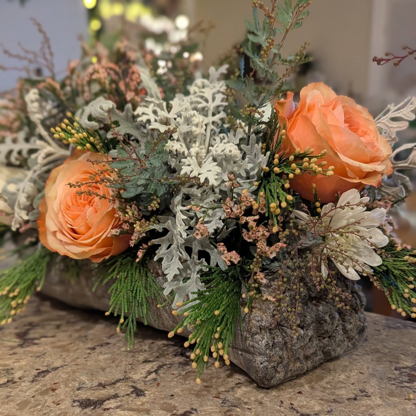 Low rustic arrangement with peach roses, cream blooms, and textured evergreen foliage in a bark-like container