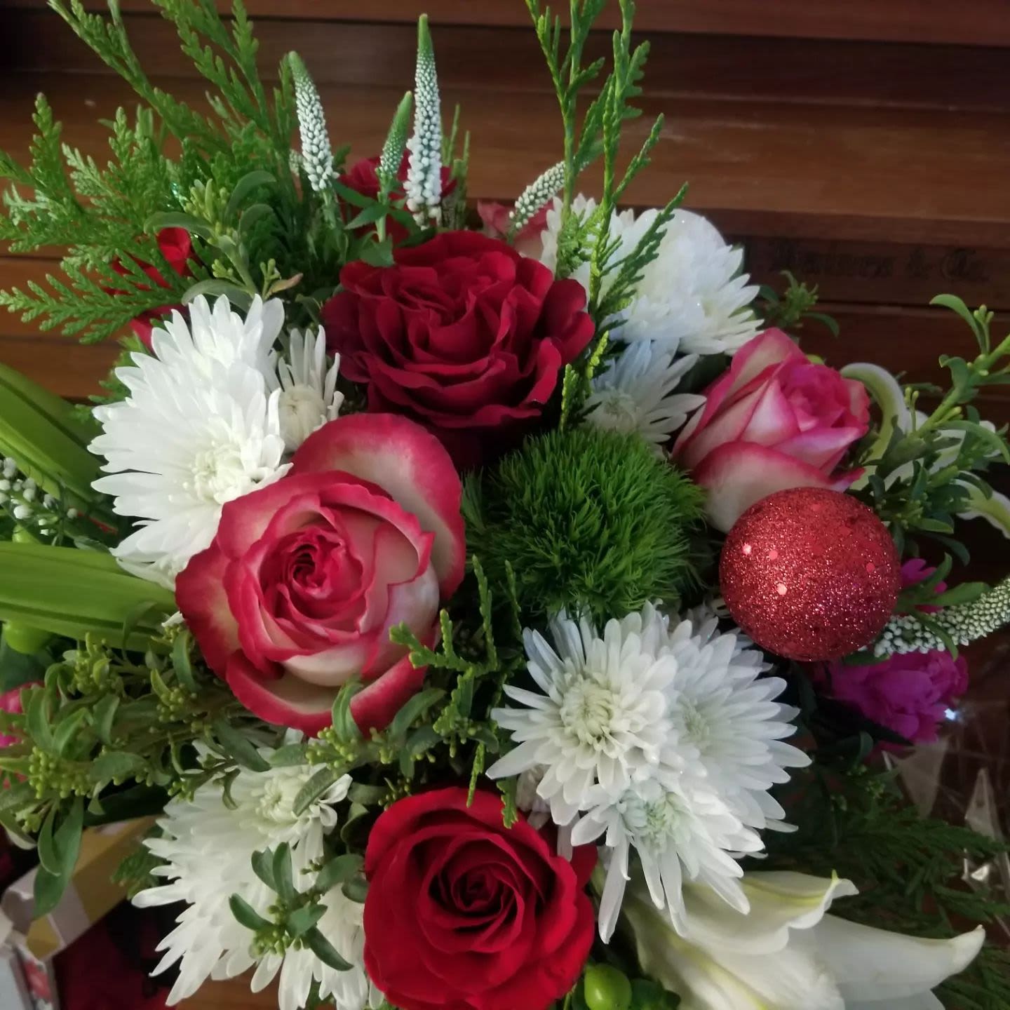 Red and white rose and mum arrangement with evergreens and a red glitter ornament ball.