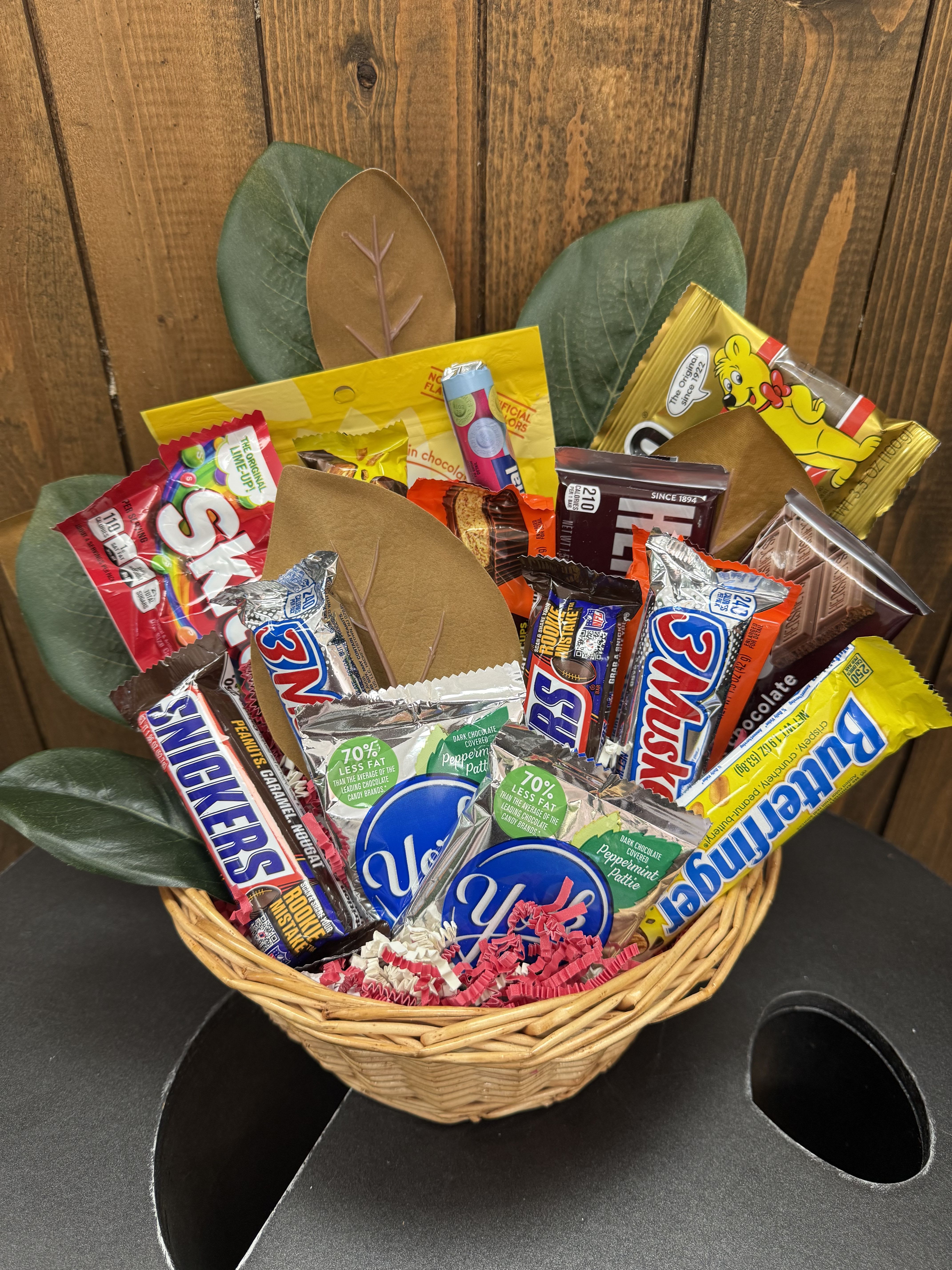 Basket of assorted candy bars with faux leaves behind it