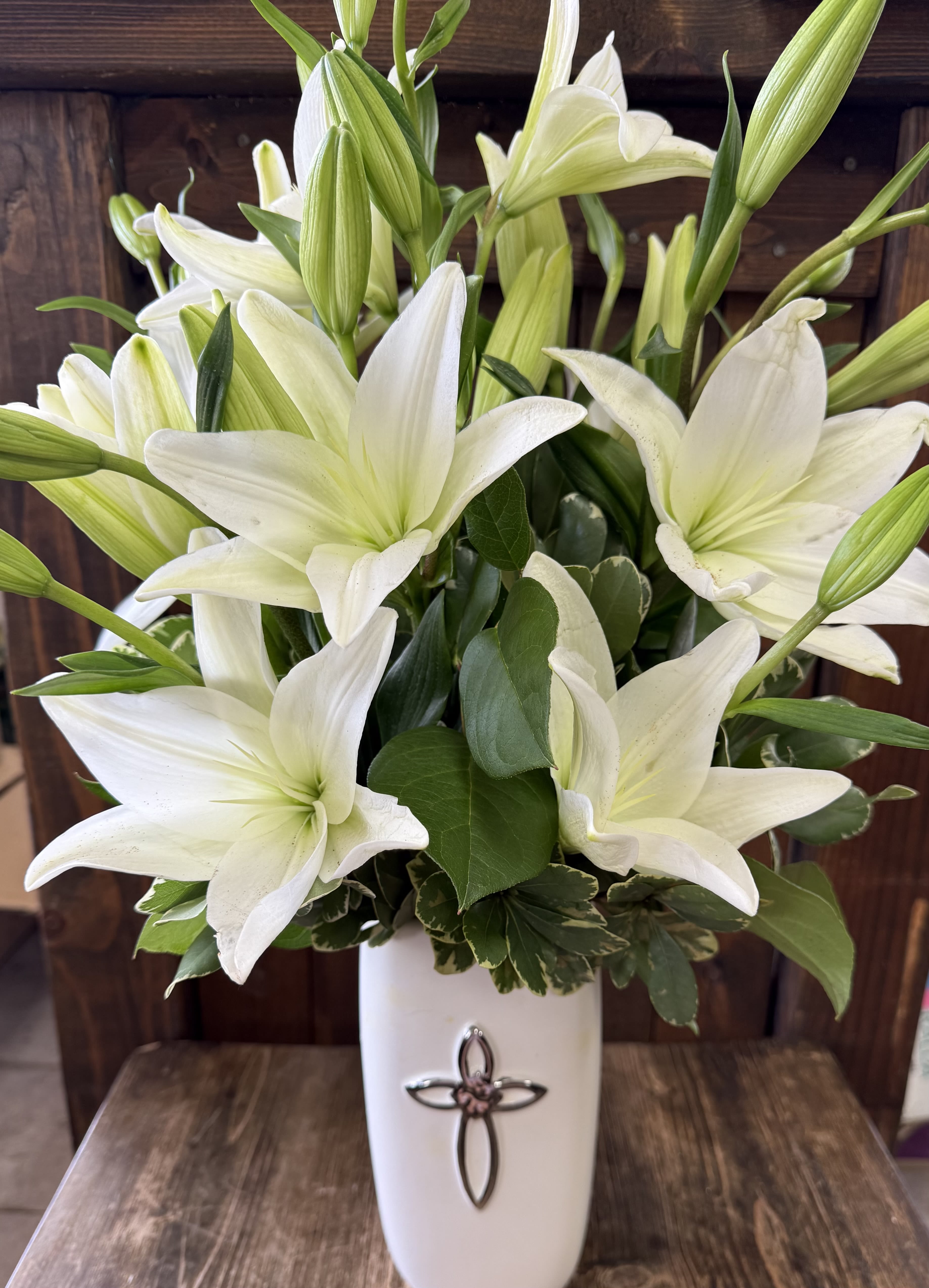 White lilies arranged in a tall white vase with a cross emblem