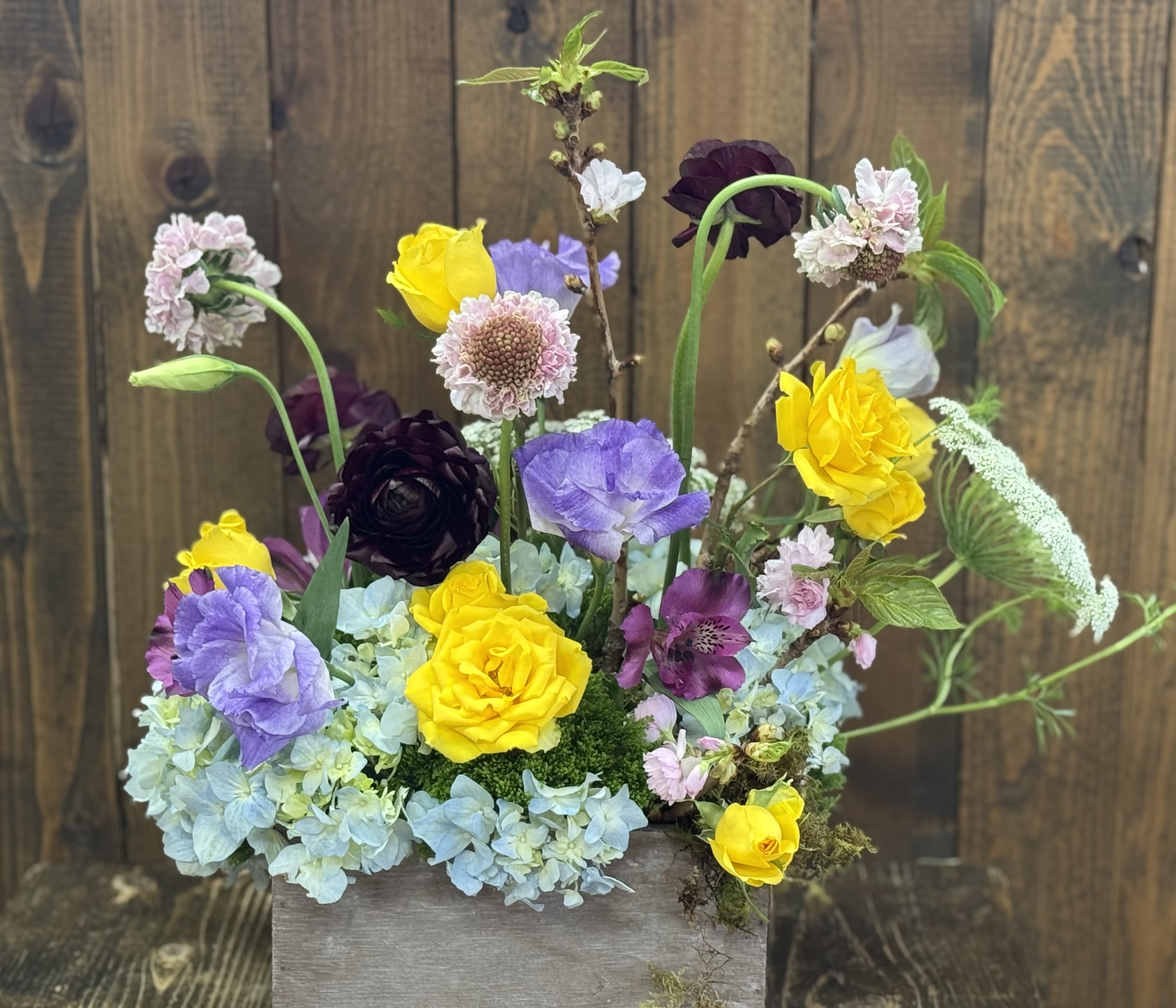 Mixed bouquet in a wooden box with yellow, purple, pink, and blue flowers