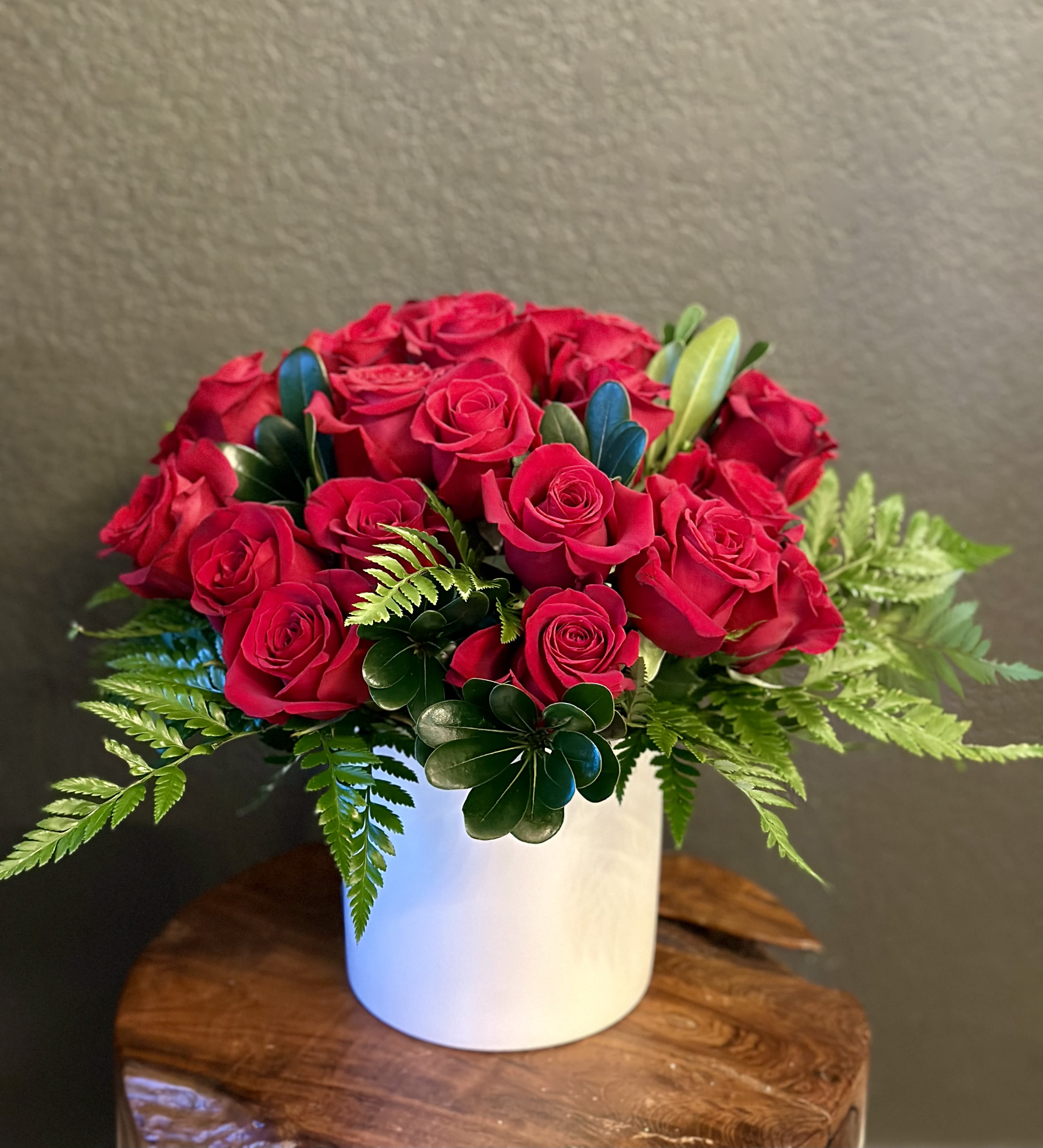 Red roses arranged in a white cylindrical vase with fern accents