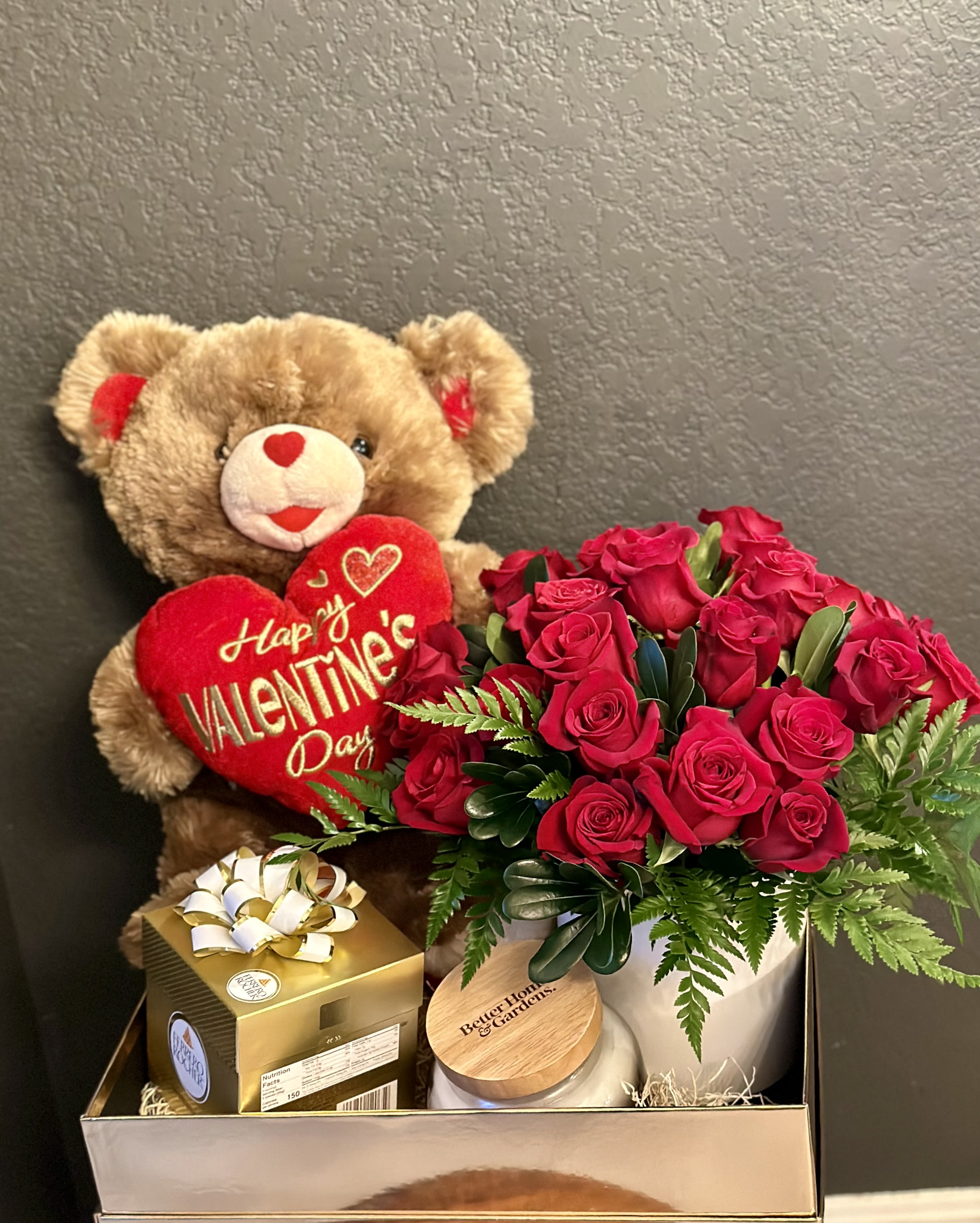 Teddy bear with a Valentine heart beside red roses and a gift box
