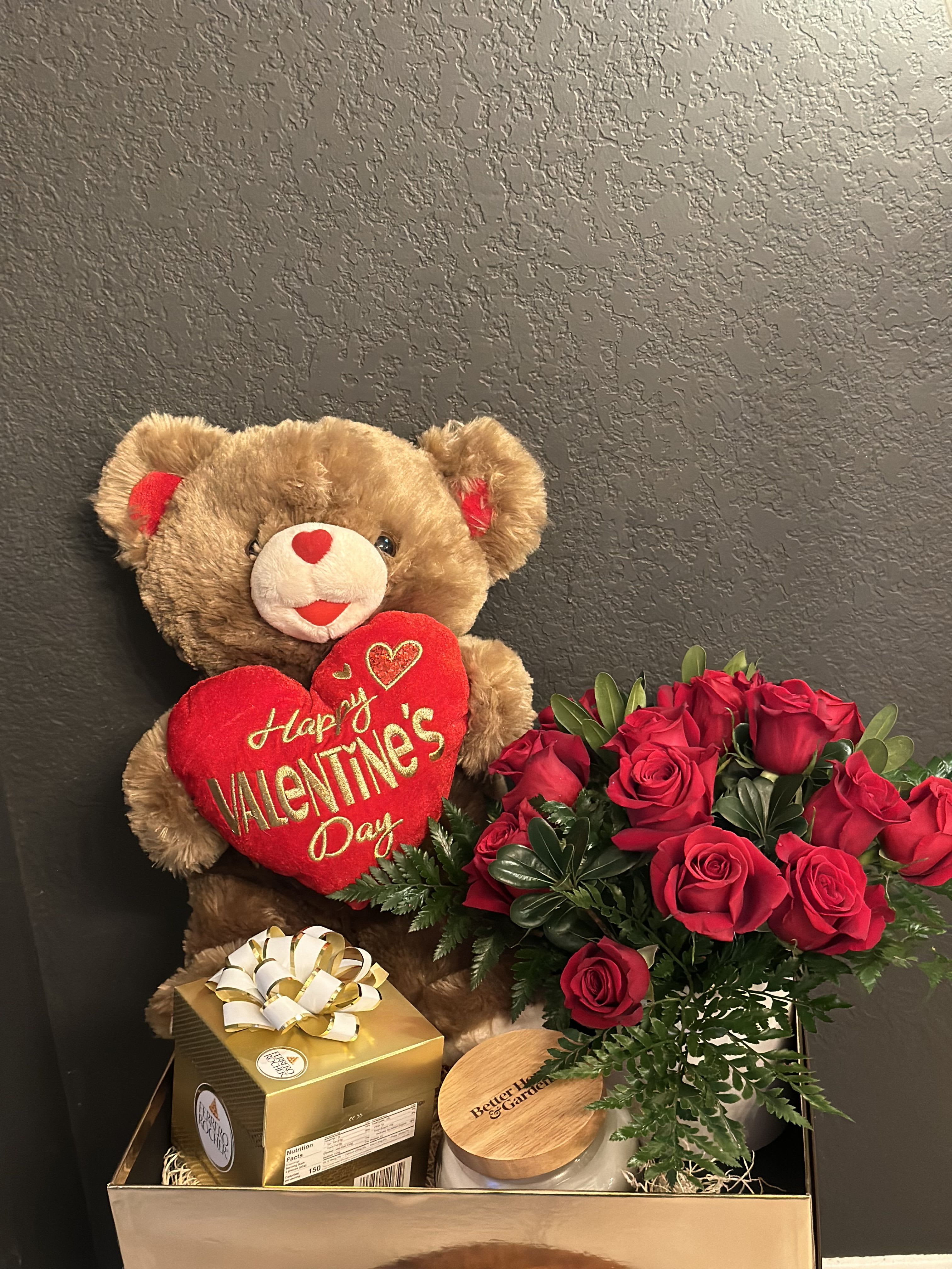 Teddy bear with a Valentine heart beside red roses and gift boxes