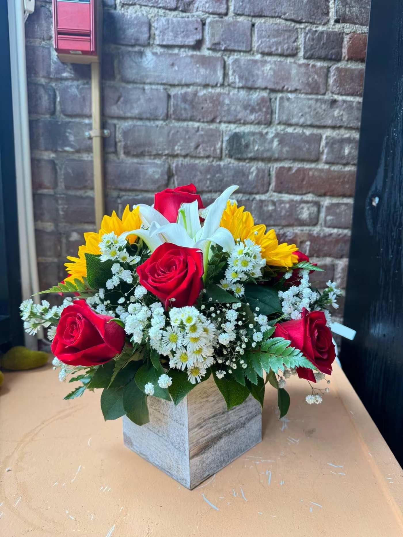 Bouquet of red roses, white lilies, and yellow daisies in a square wooden vase